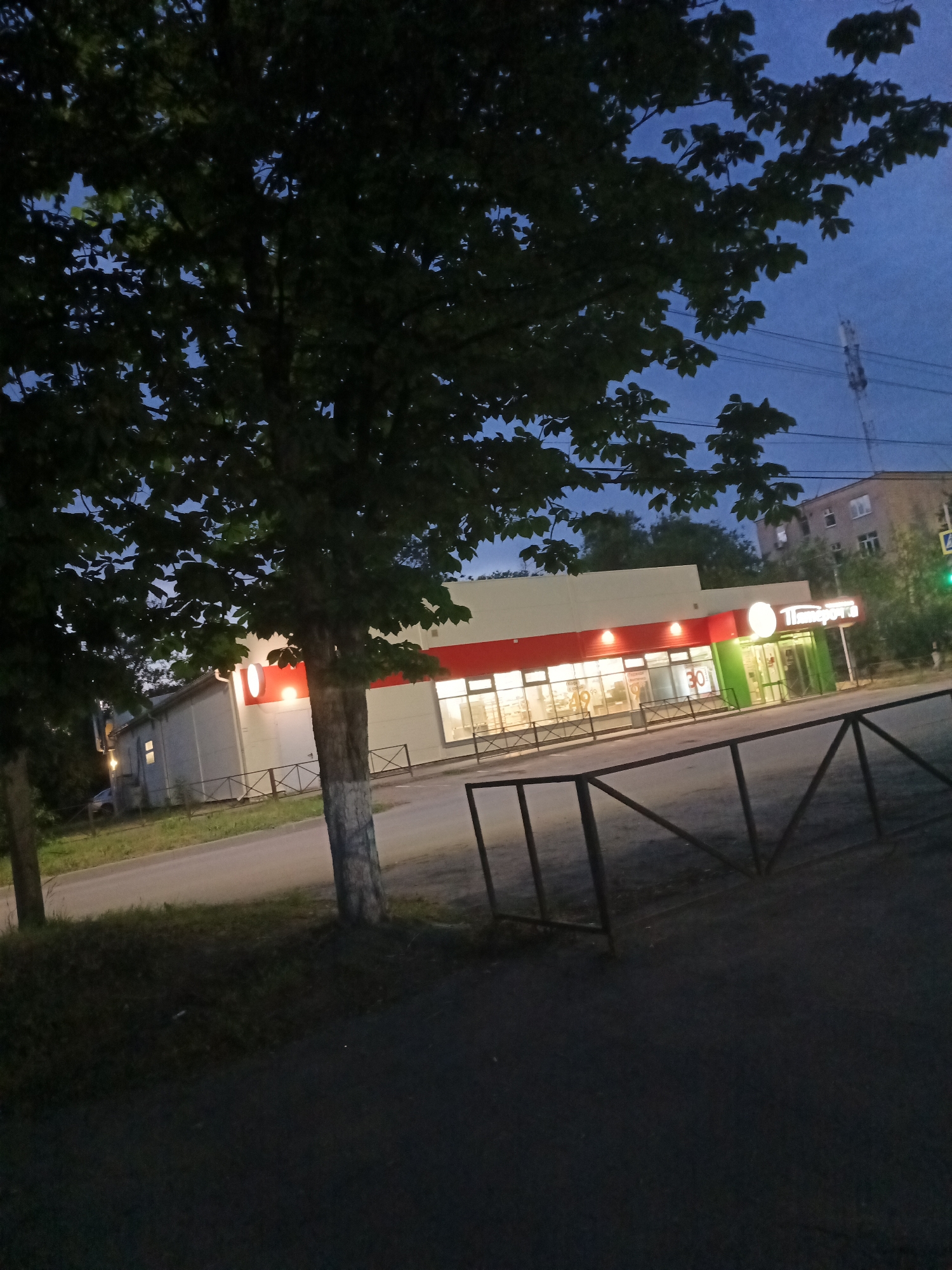 Dusk street corner with Cyrillic storefront and tree-lined sidewalk
