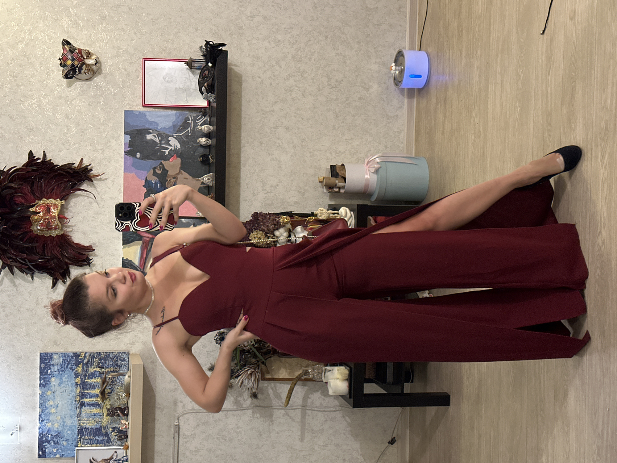 Woman takes selfie in maroon jumpsuit near decorative display