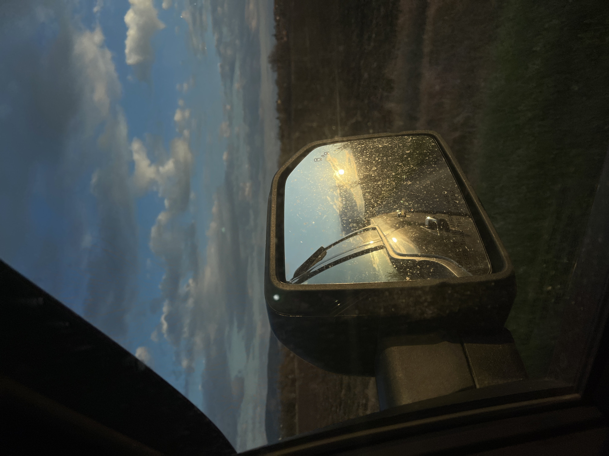 Car mirror reflects cloudy landscape in Bulgarian village
