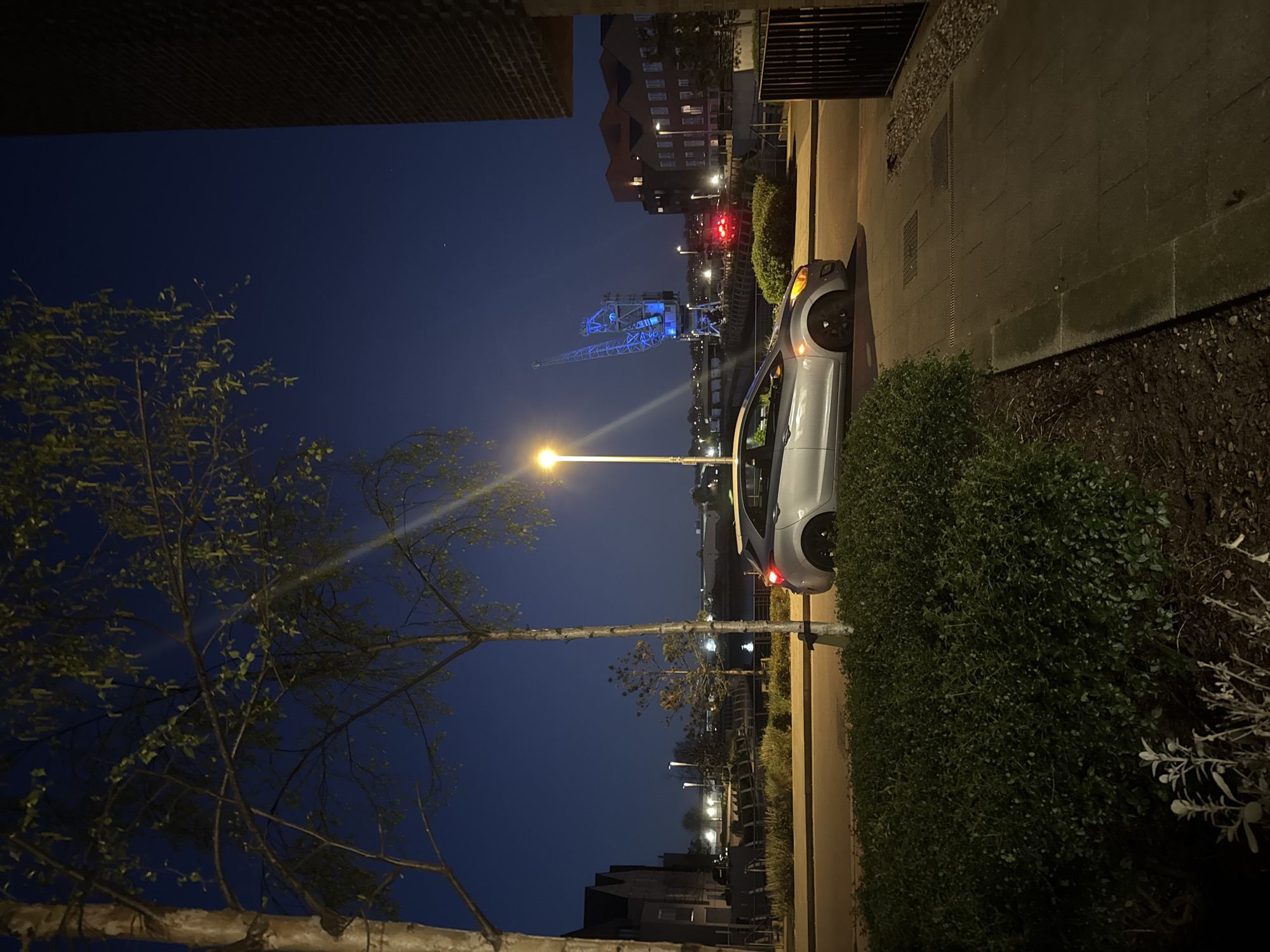 Car parked on Rochester street with illuminated crane visible