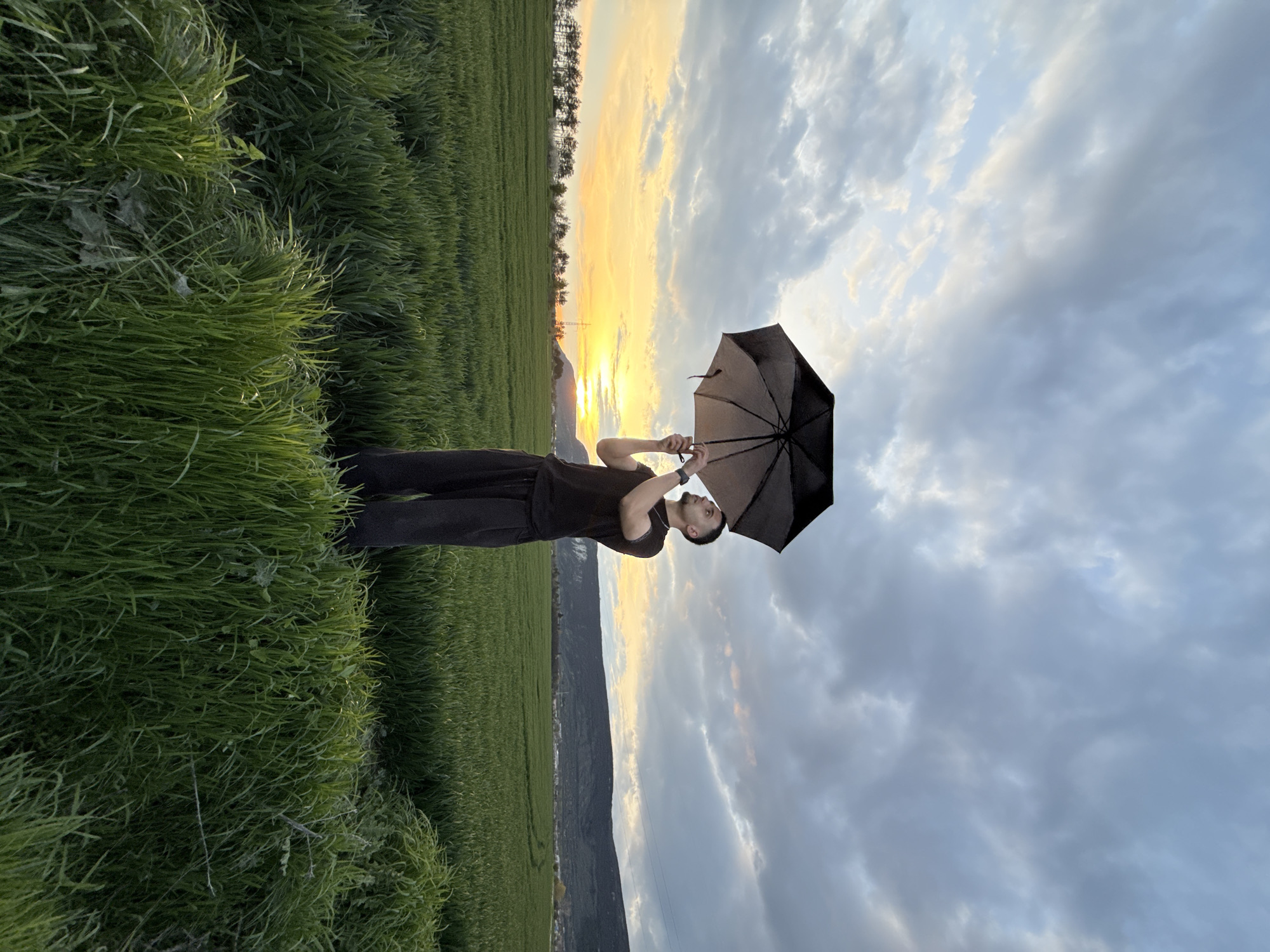 Man with umbrella stands in Bulgarian field at sunset