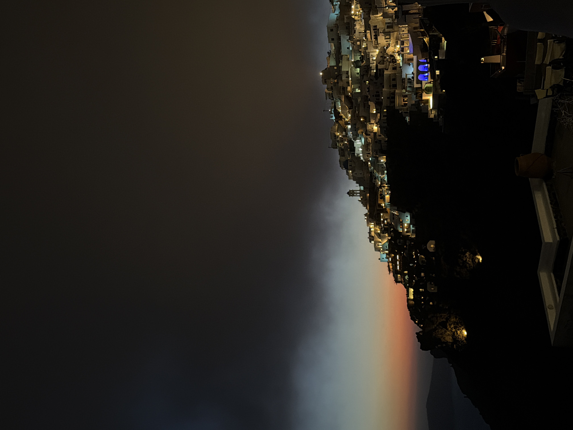 Evening lights illuminate cliffside buildings in Thira, Greece