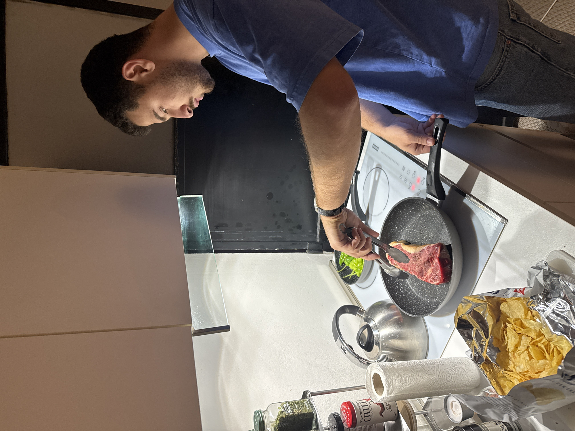 Young man cooks steak dinner in Milan kitchen