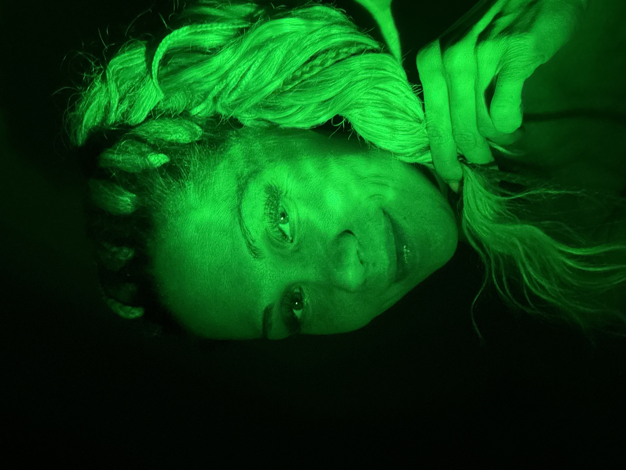 Green-lit portrait captured showing braided subject with neutral expression
