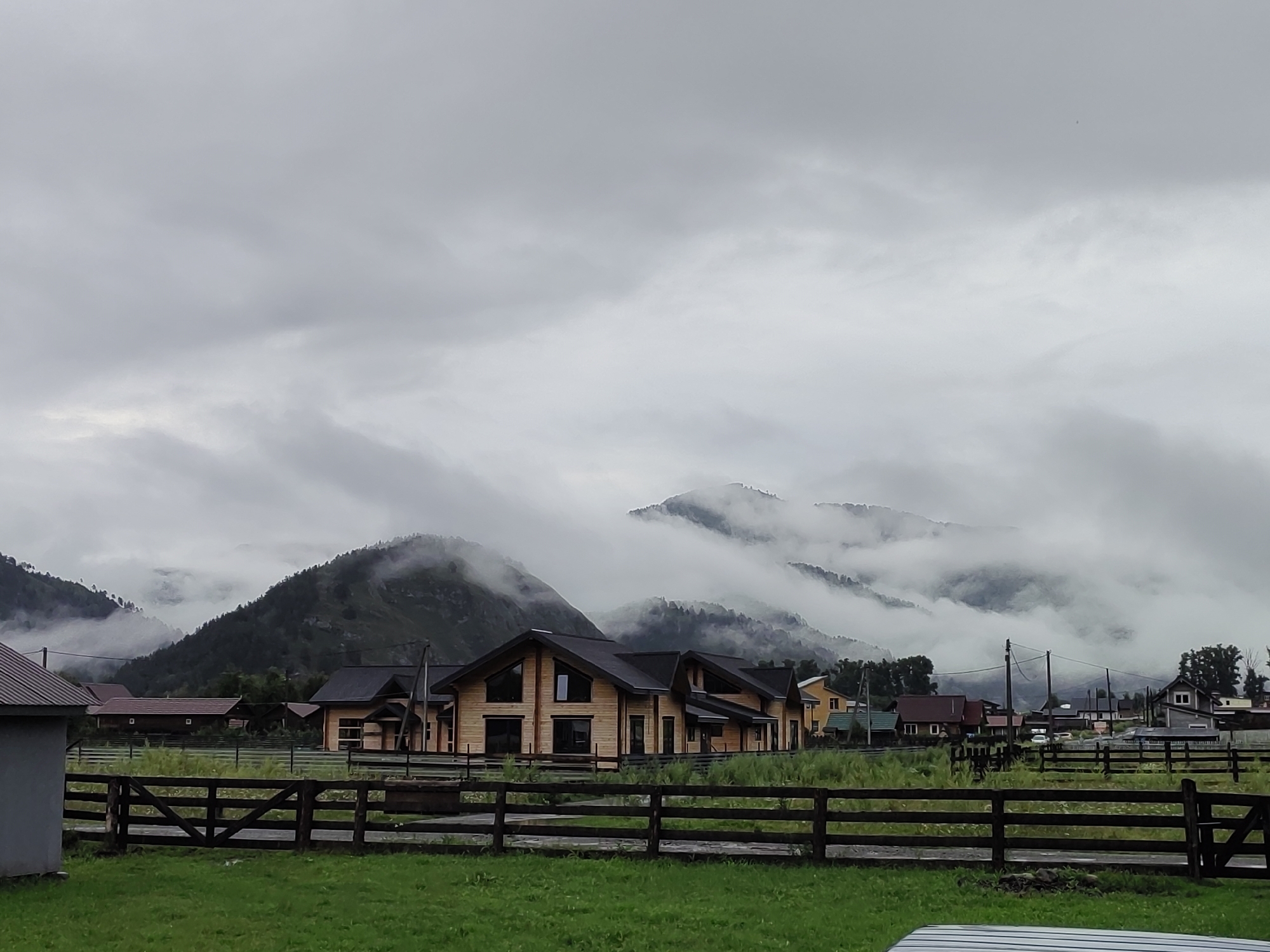 Green fields and wooden fences under overcast skies in Anos