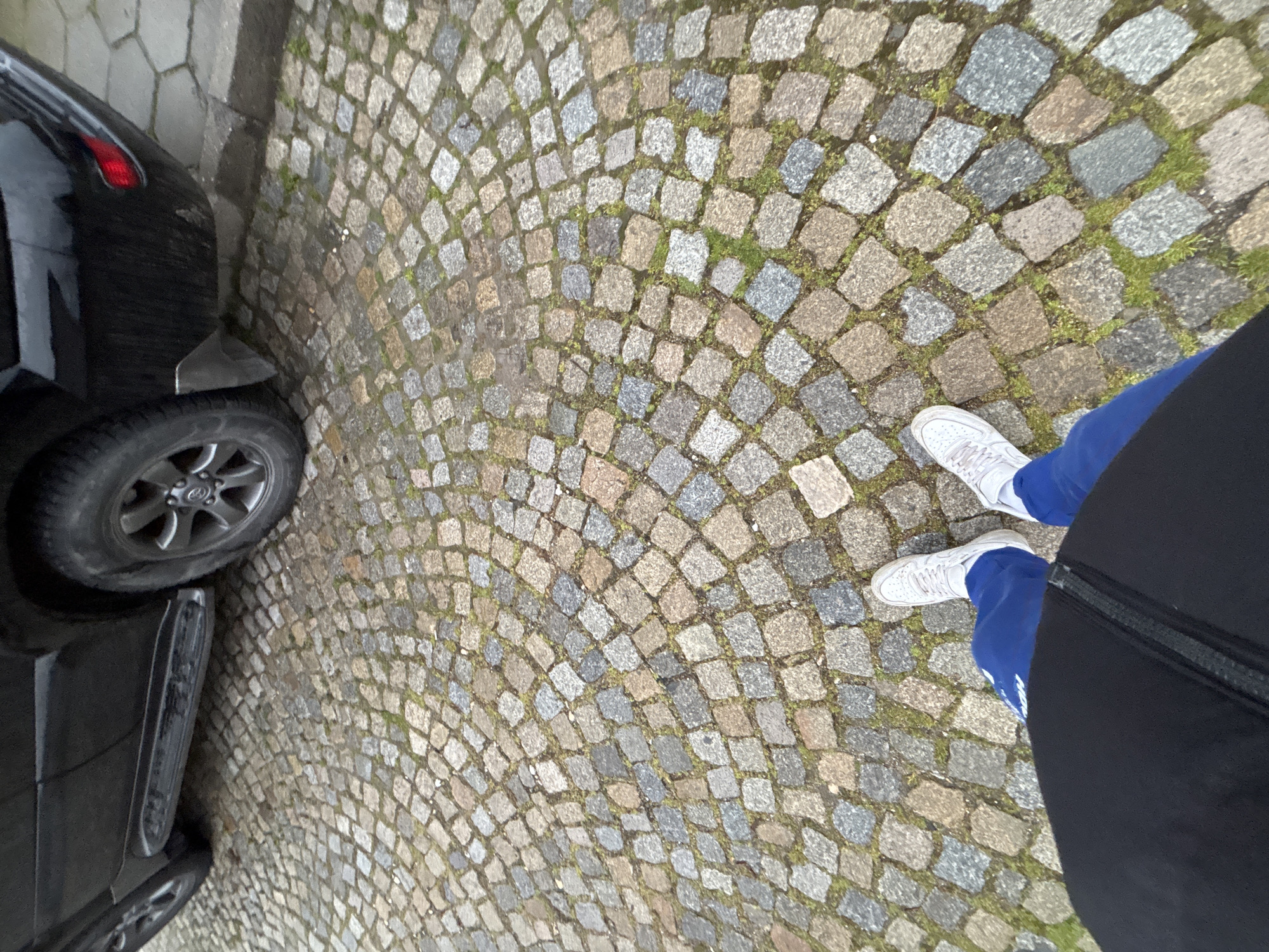 Person stands beside black car on cobblestone street in Sopot