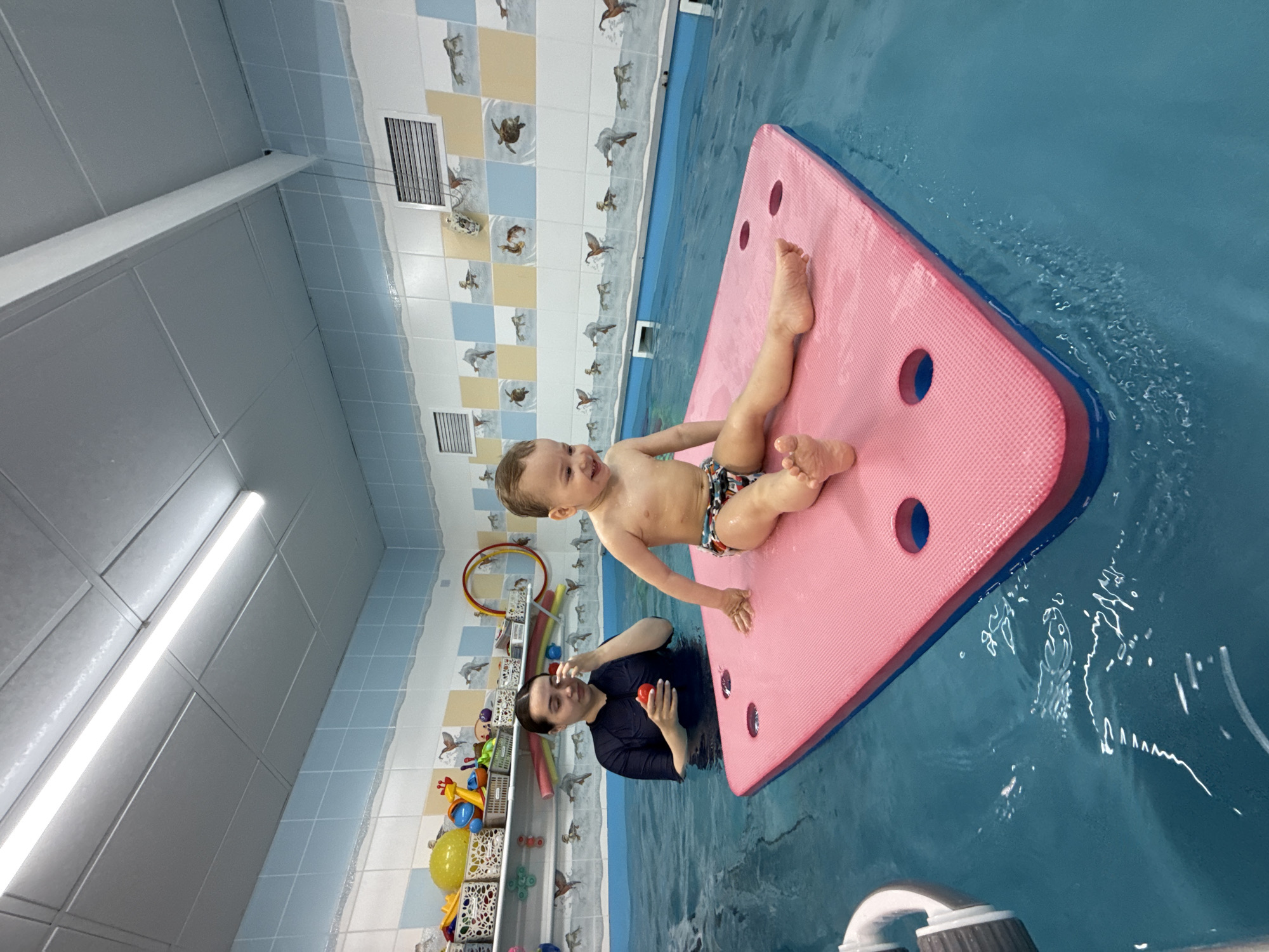 Toddler enjoys swimming activities on pink float in Rusanovo pool