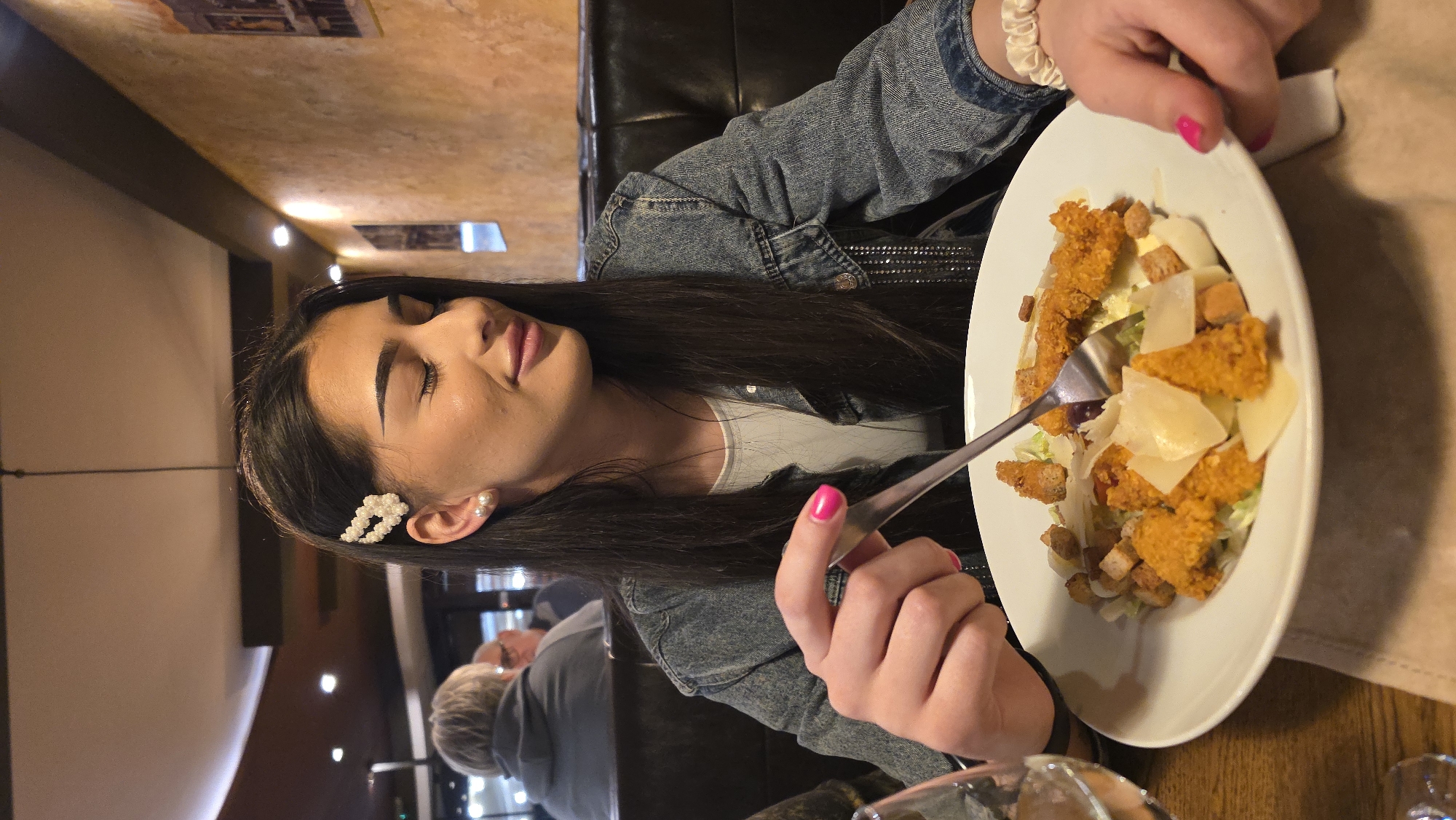 Woman dines alone at dimly lit restaurant wearing denim