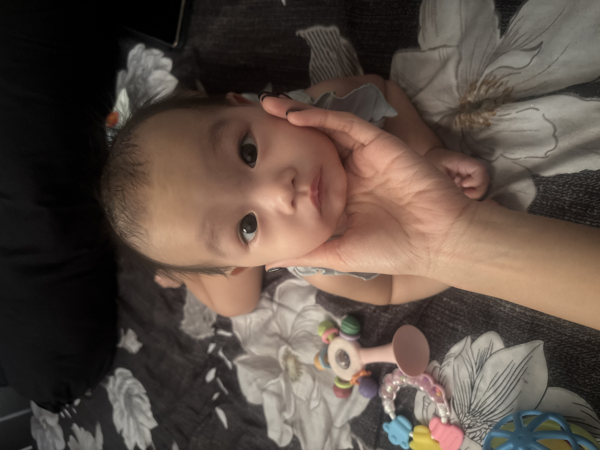 Infant on patterned bed, cheek cradled by a gentle hand