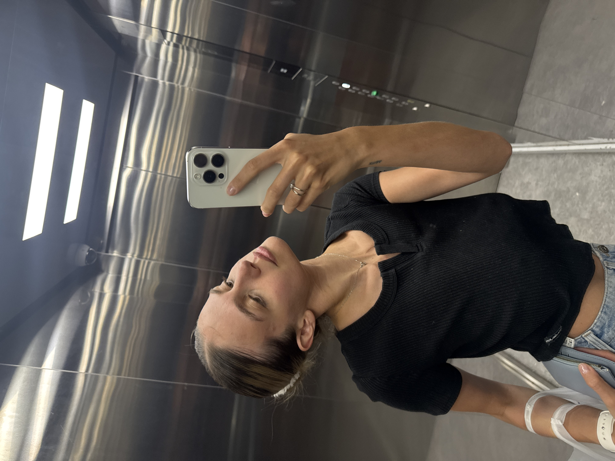 Woman with medical wristband takes elevator selfie, drinks vitamin water