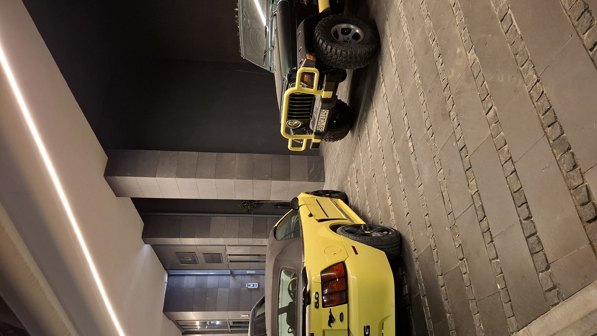 Yellow Mustang, dark Jeep parked on stone paving in Budva