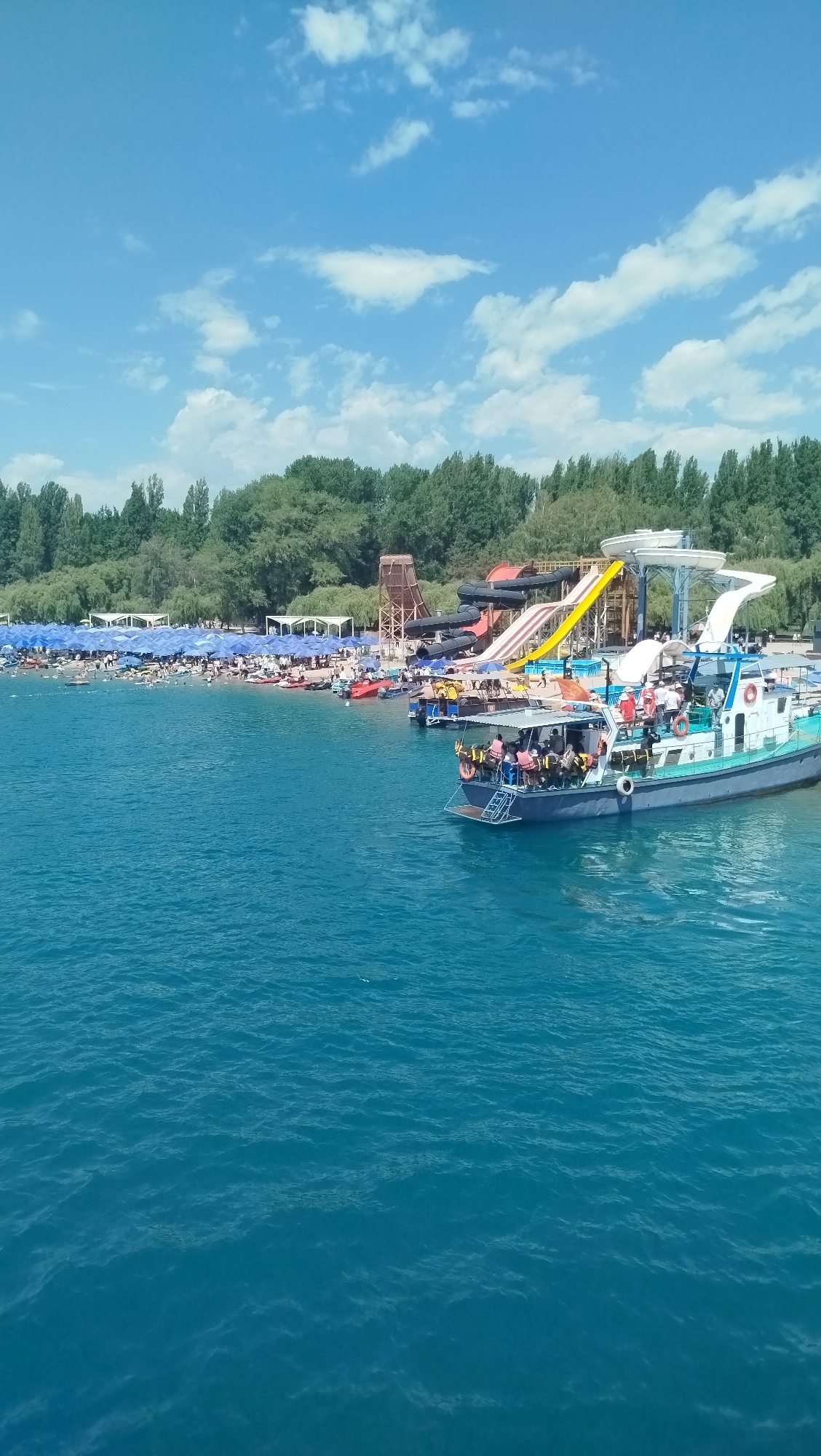 Busy day at a waterfront amusement park with boats and a Ferris wheel