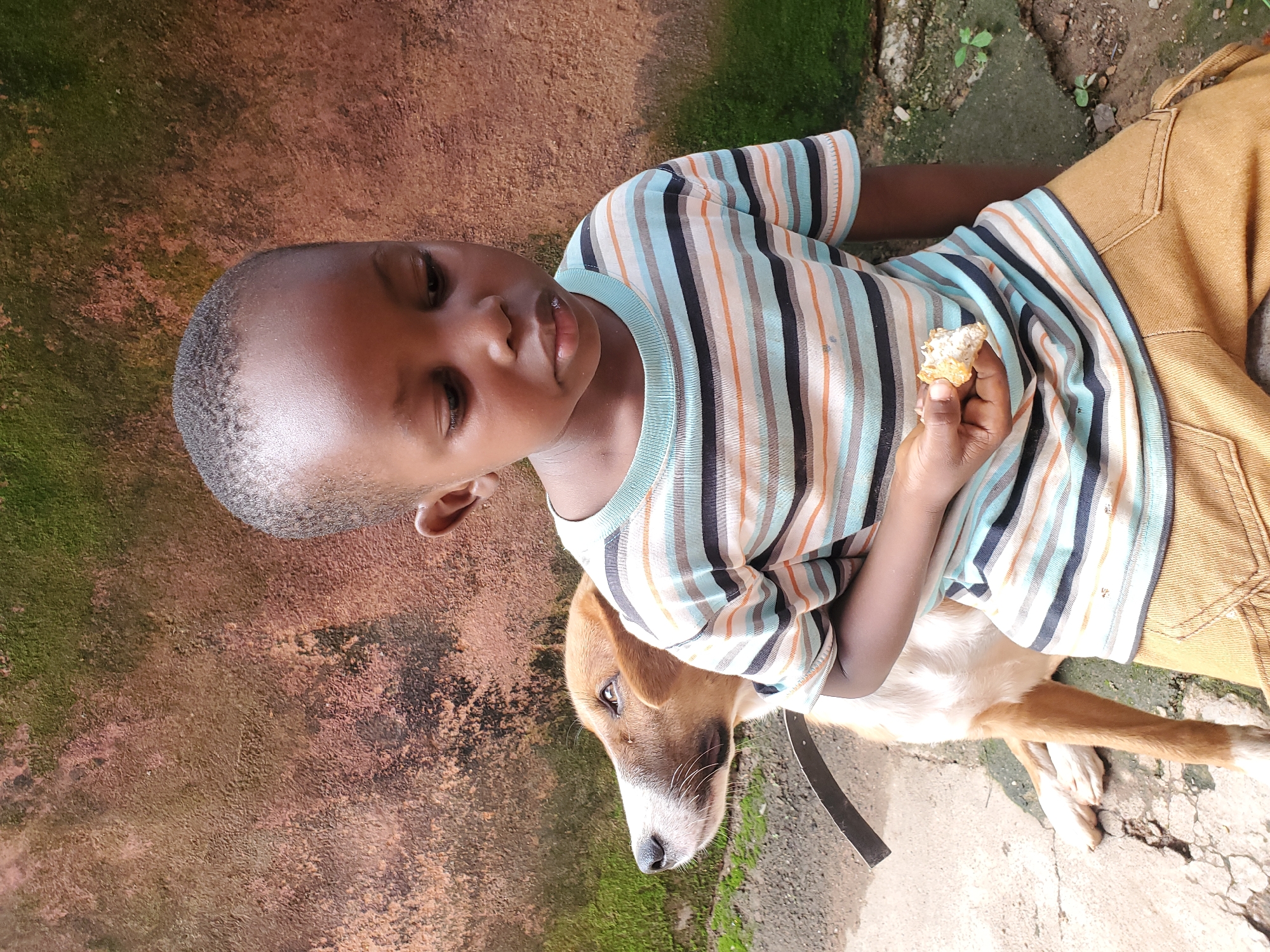 Kid shares a snack moment with a dog in Jos