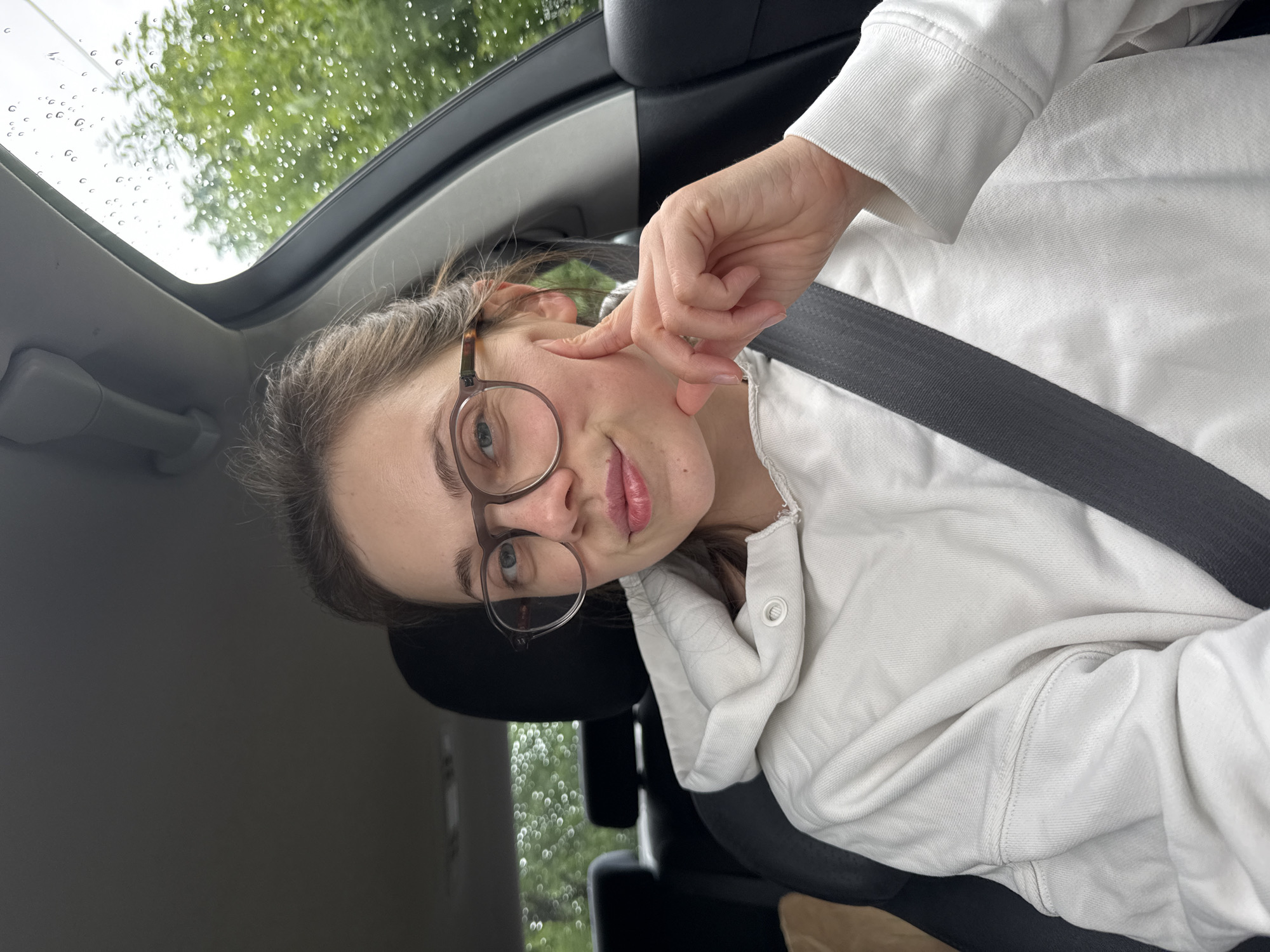 Woman in white hoodie sits in car in Vrchlabí