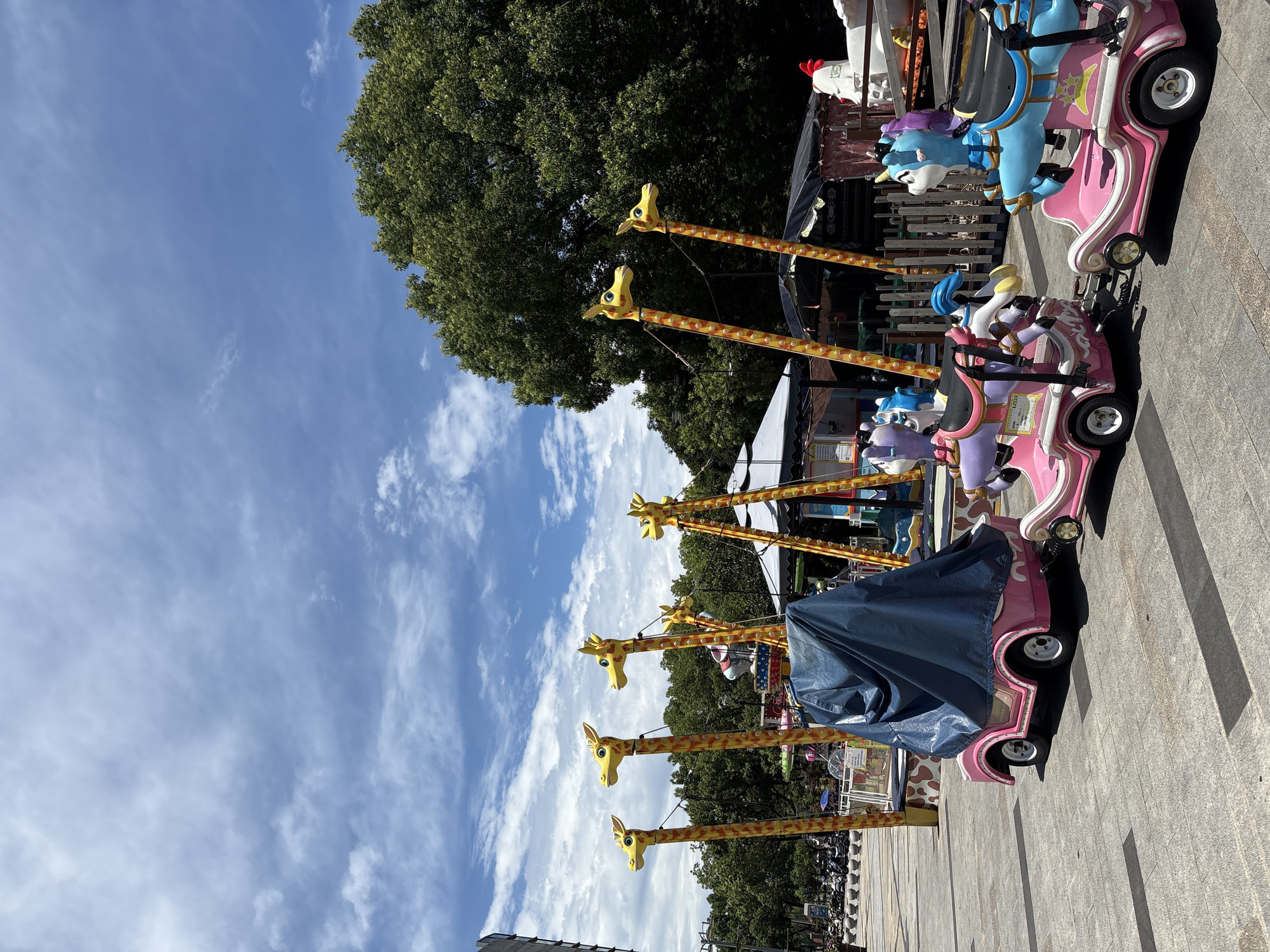 Minhang street scene: amusement rides, vendors, and a cartoon-wrapped Tesla