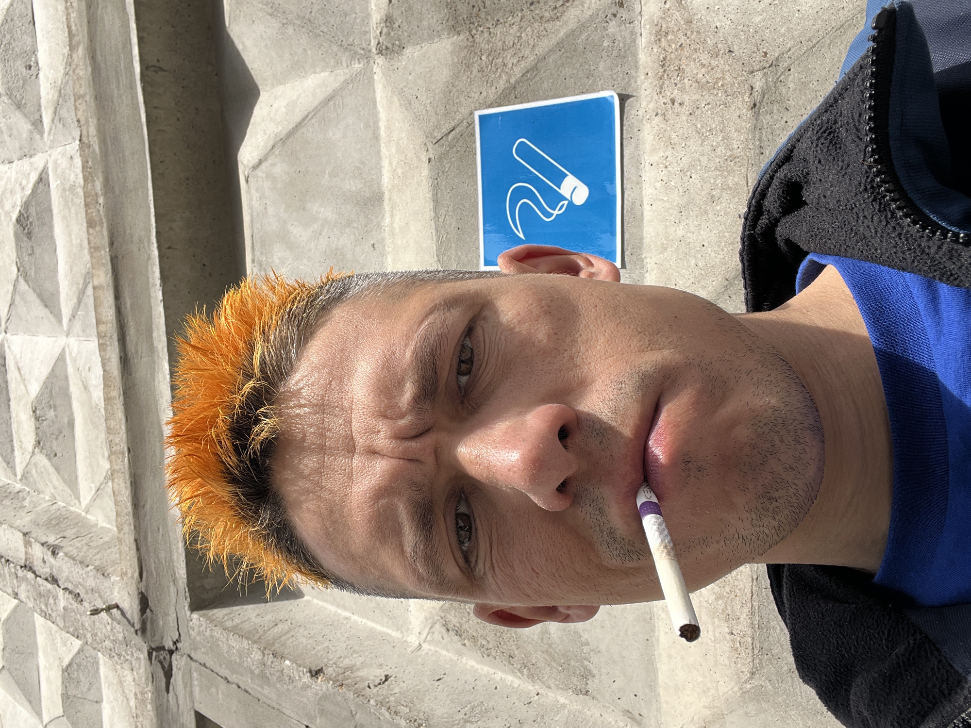 Orange-haired man smoking cigarette near concrete wall in Chaikovsky