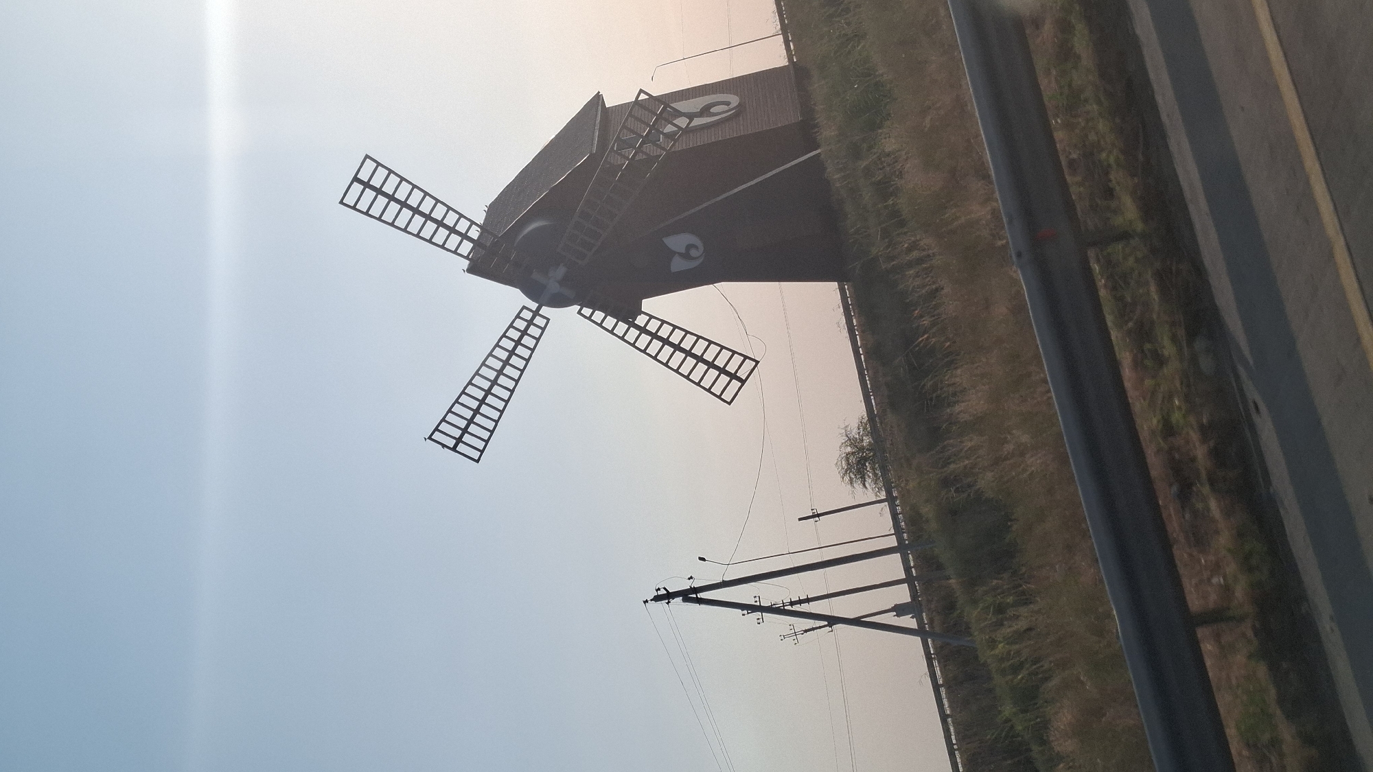 Wooden windmill on a grassy hillside under a hazy Shymkent sky