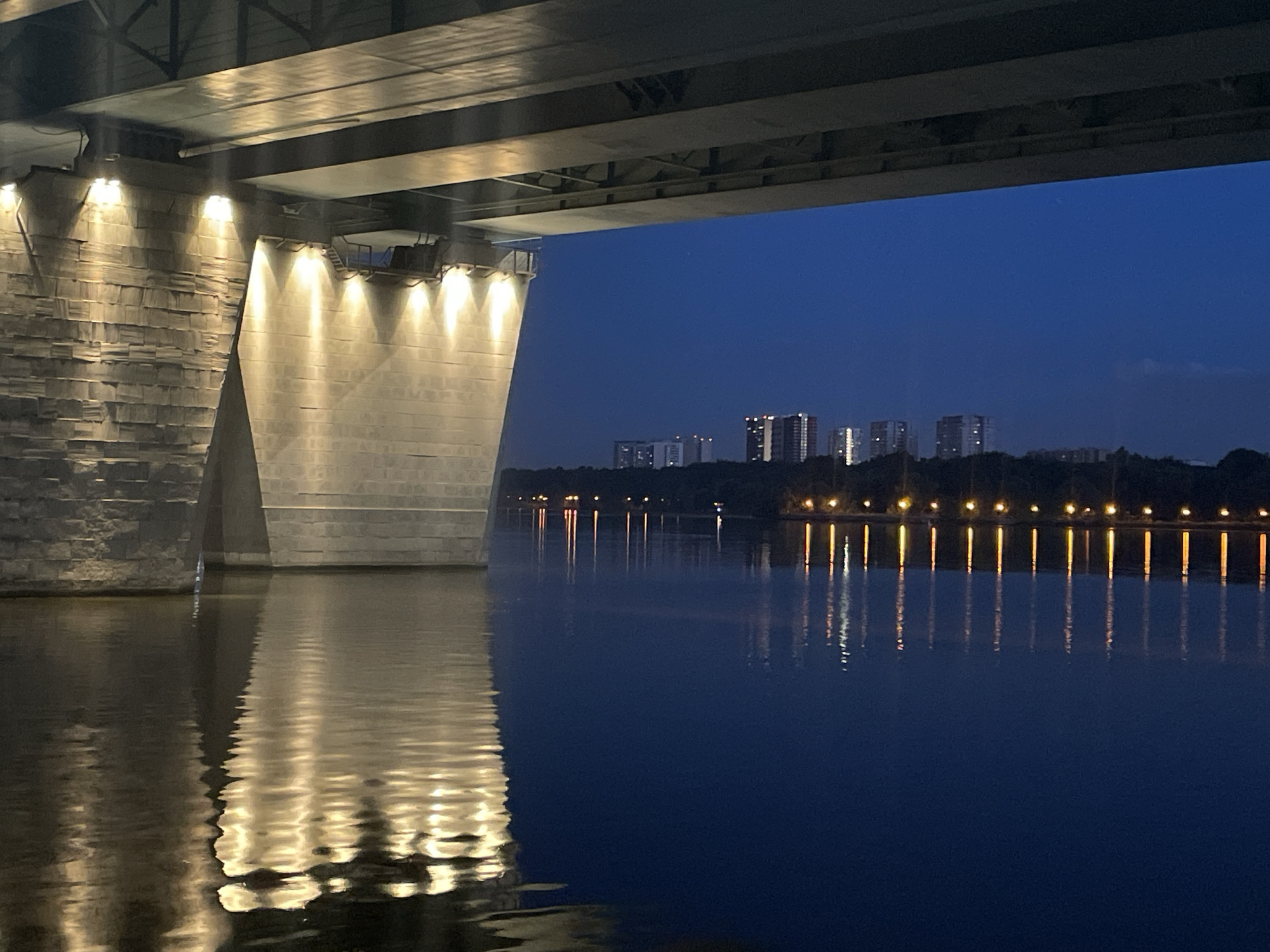 Under a bridge at dusk, Khimki Reservoir glows in warm light