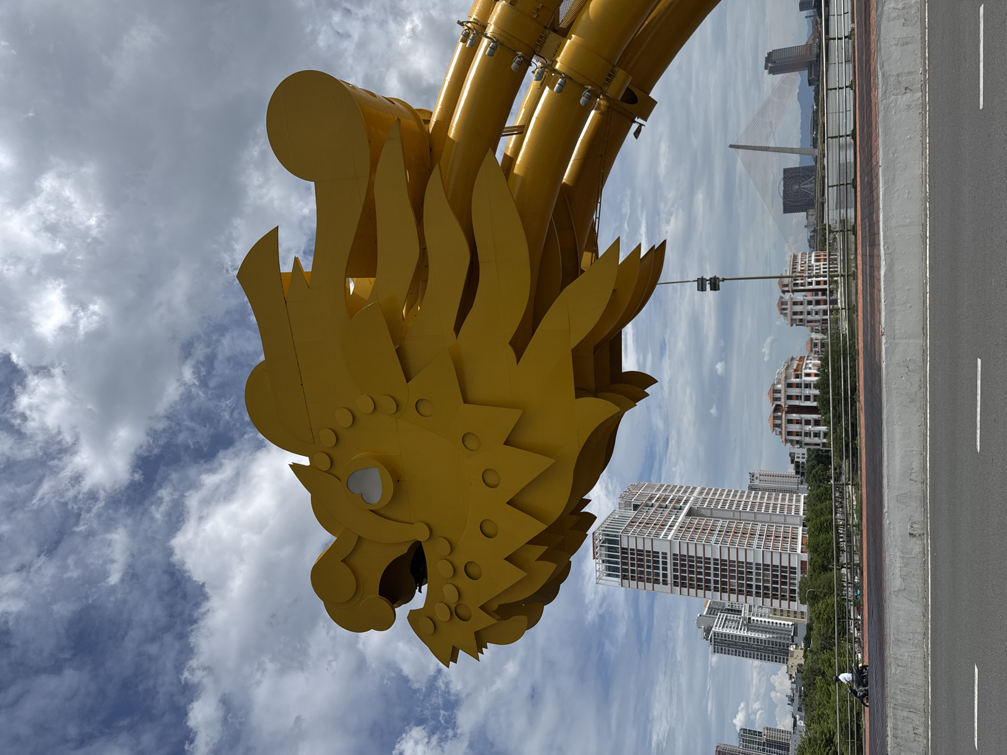 Yellow dragon sculpture on a bridge, cloudy city skyline beyond