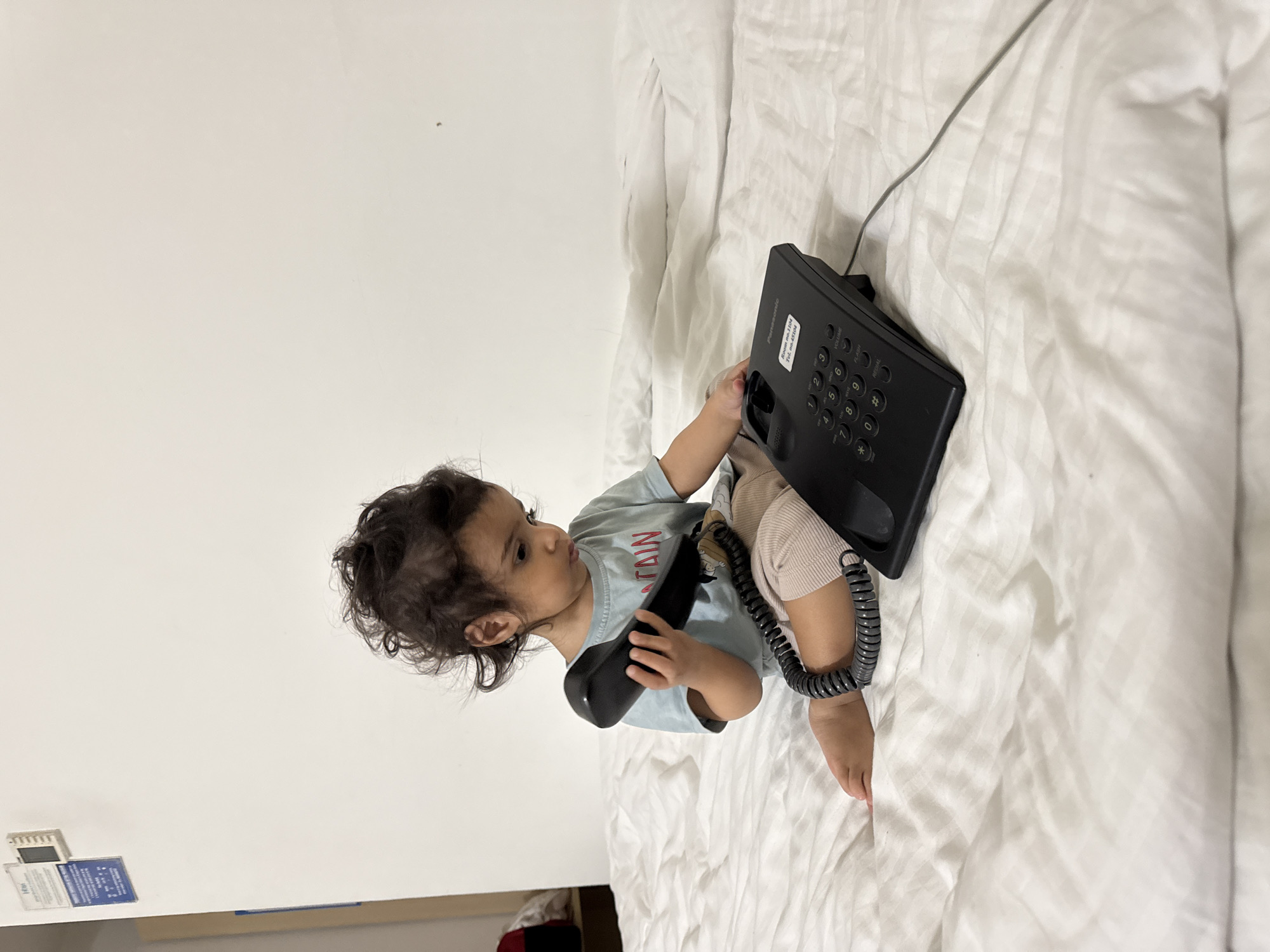 Child plays with telephone on bed in Indian home