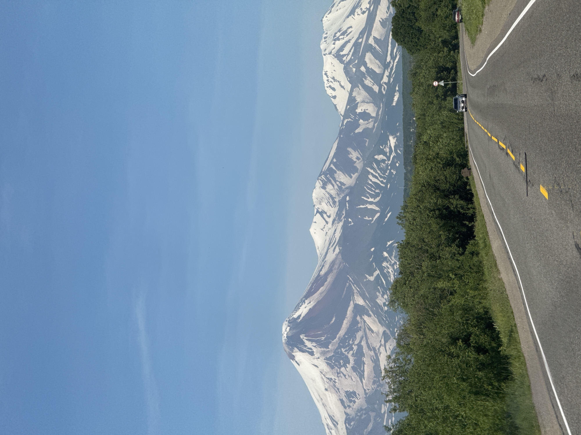 Snow-capped volcanoes loom over a curving road in Kamchatka