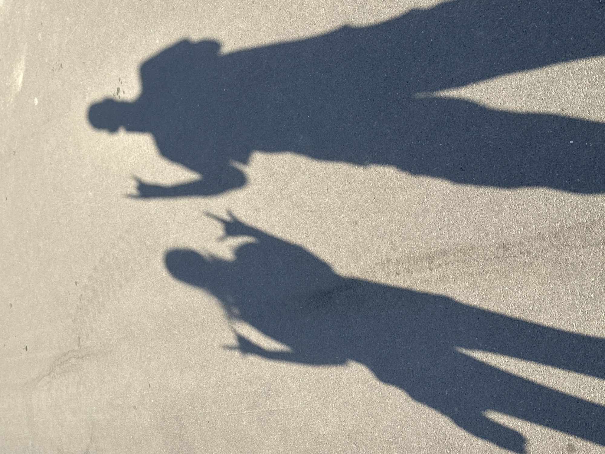 Peace sign shadow and a larger silhouette on asphalt