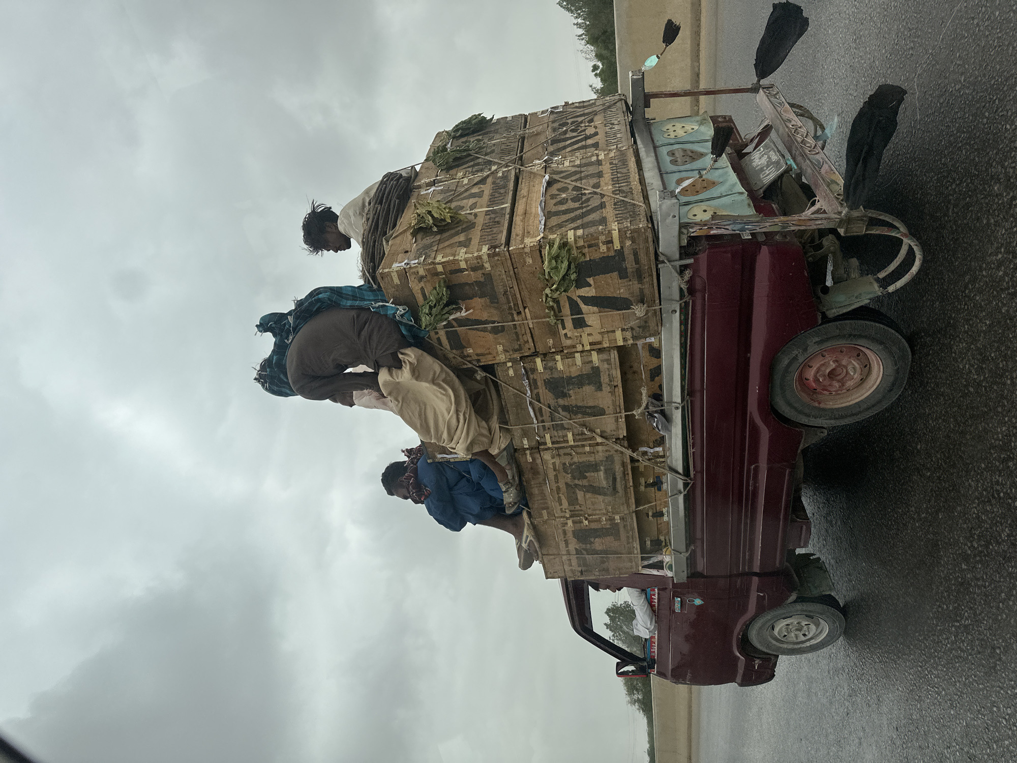 Crate-loaded pickup truck navigates wet Karachi roads in overcast conditions