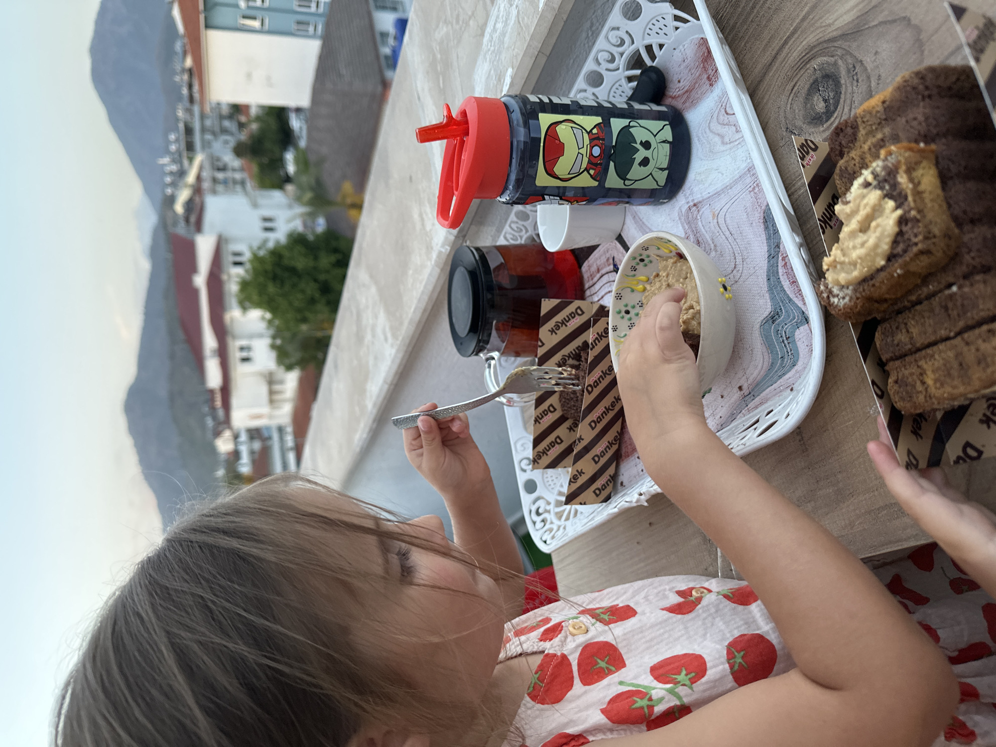 Child dines on terrace as mug held against mountain view
