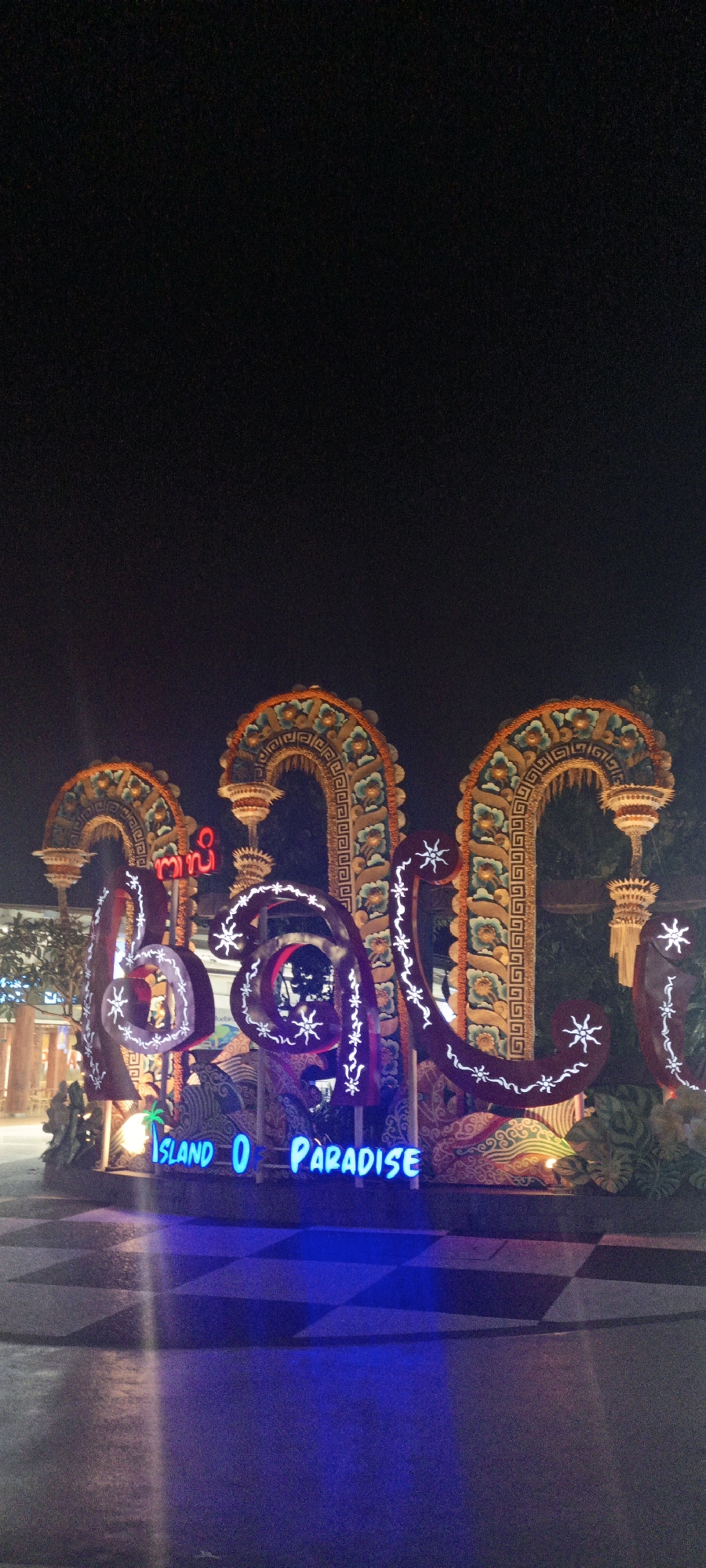 Neon 'Bali Island of Paradise' sign glowing at night in Kuta