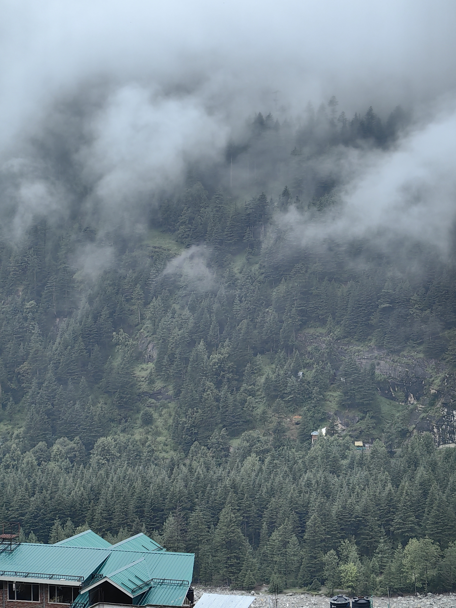 Vashisht under cloud cover, river, forest, and active construction