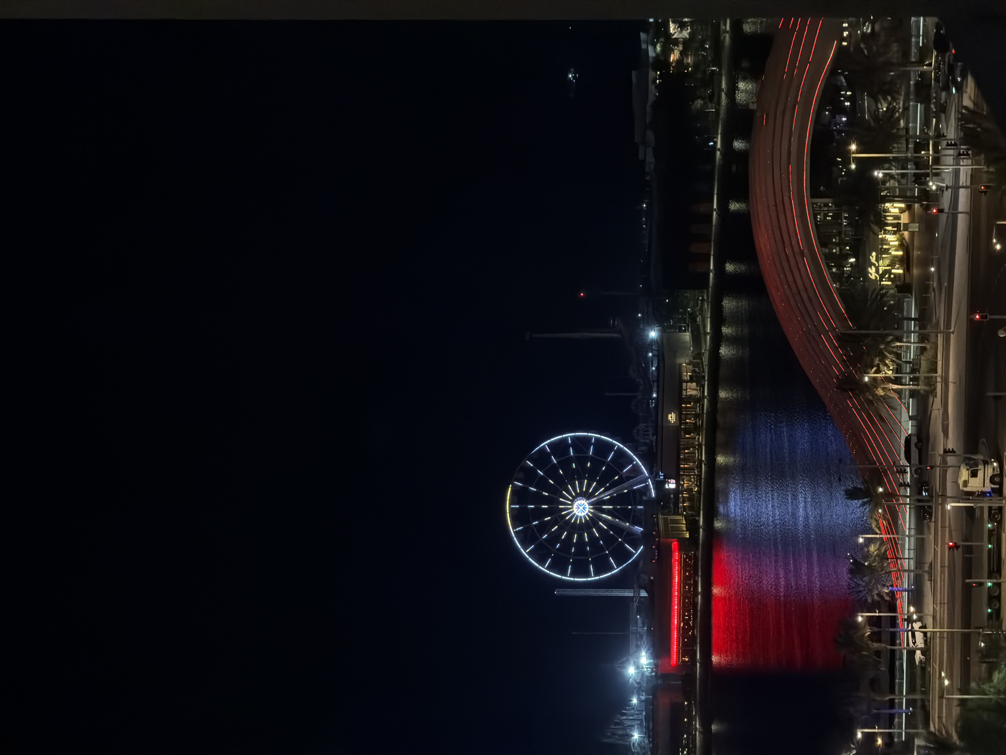 Colorful Ferris wheel lights up a city waterfront at night