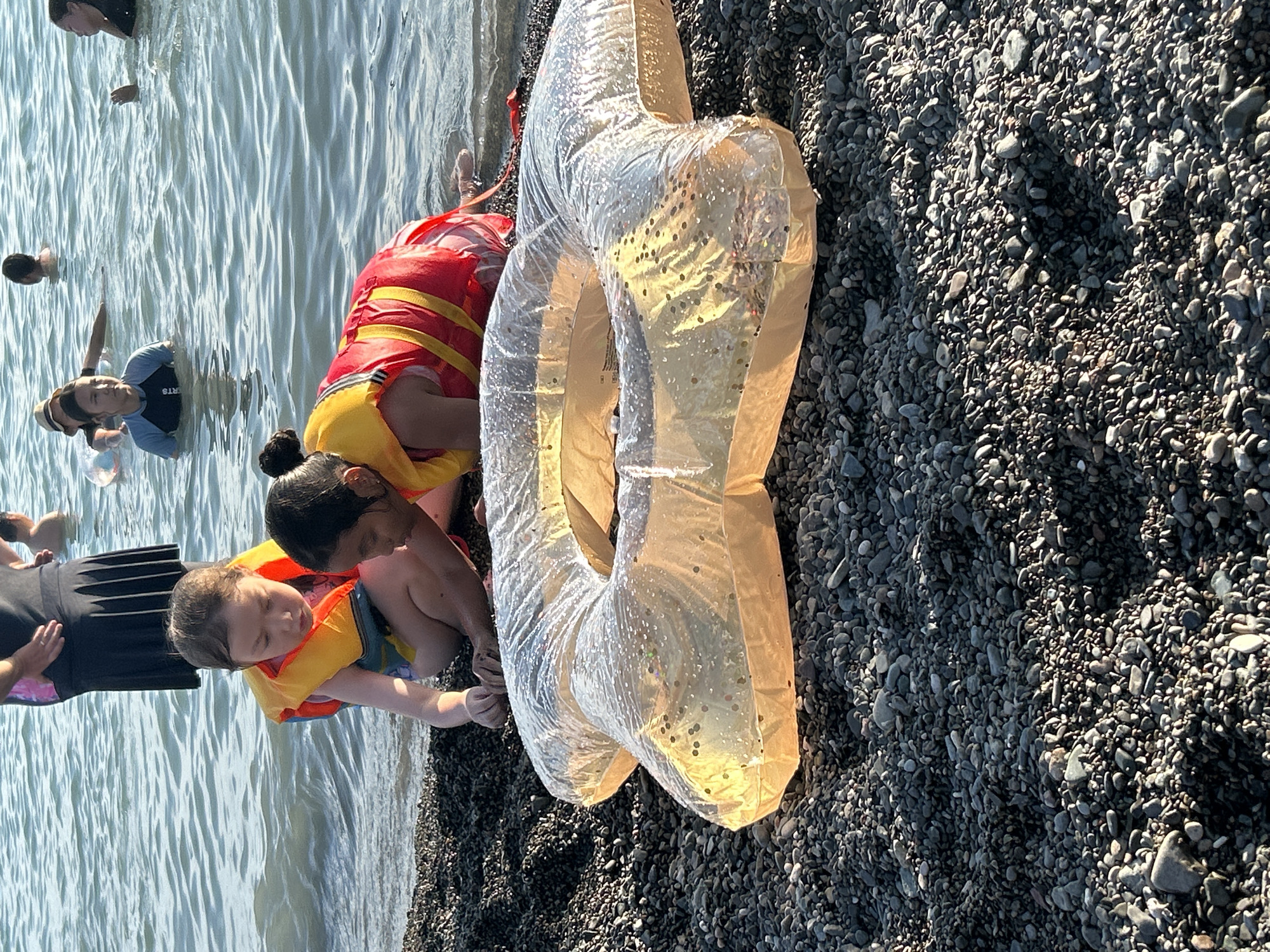 Life vests, pebbles, and a banana boat at the shoreline