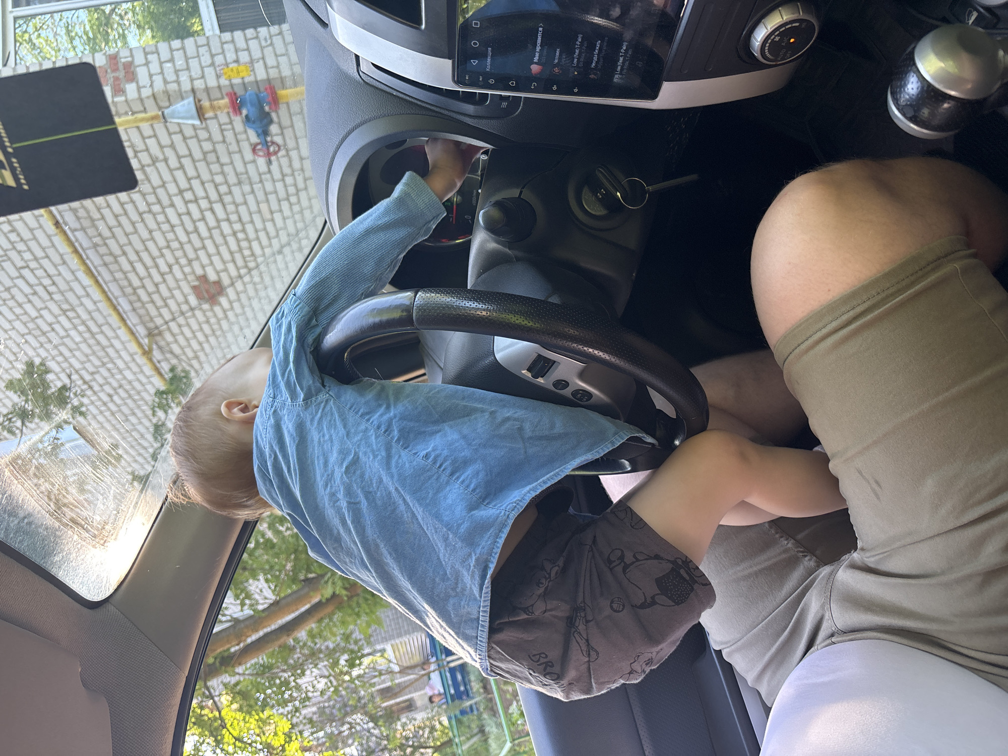 Toddler plays with steering wheel on adult's lap in Russia