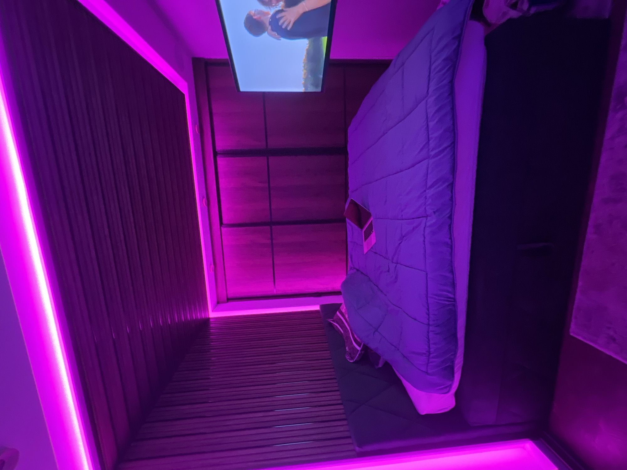 Purple-lit room with TV showing embrace scene in Varna