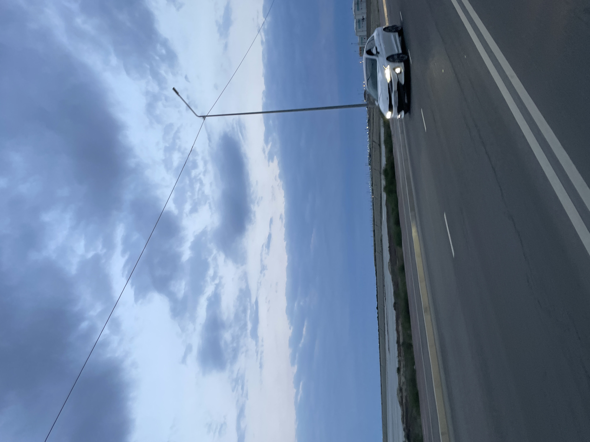 White sedan on a stormy Kazakh road, headlights cutting through overcast skies.