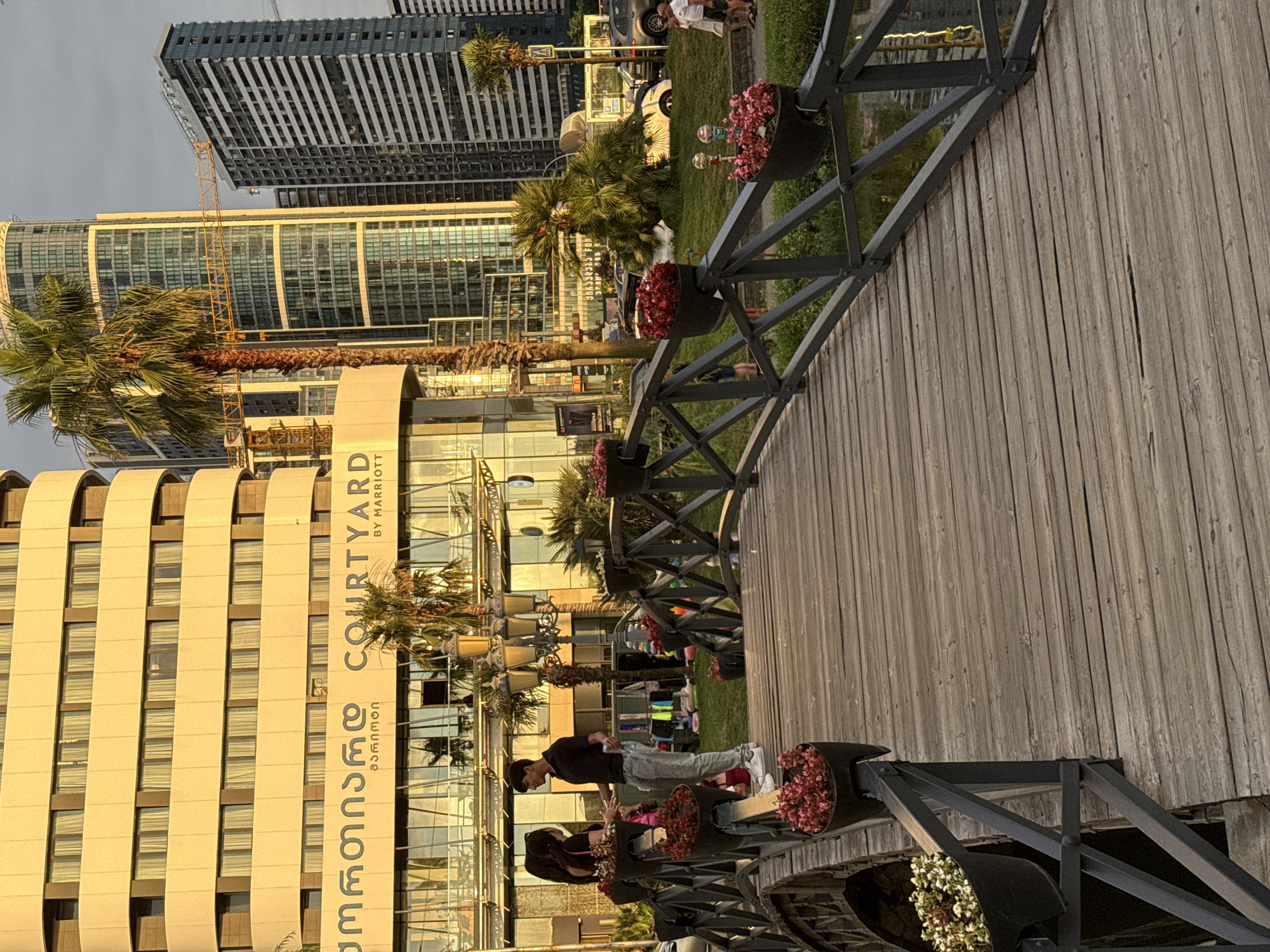 Urban streetscape mixes pagoda rooflines, modern towers, and a flower-lined bridge