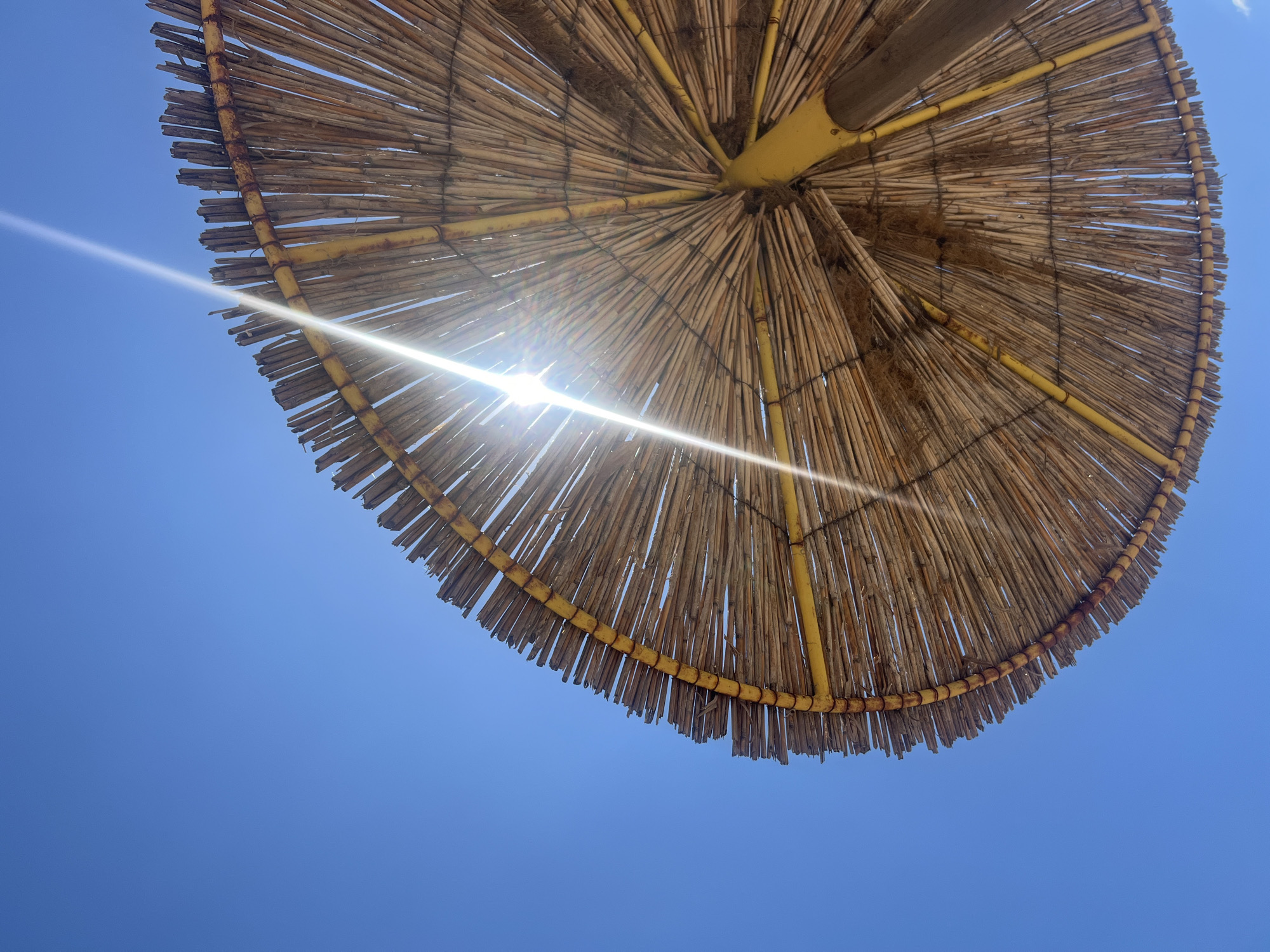 Slow beach morning under a straw umbrella, ocean in view.
