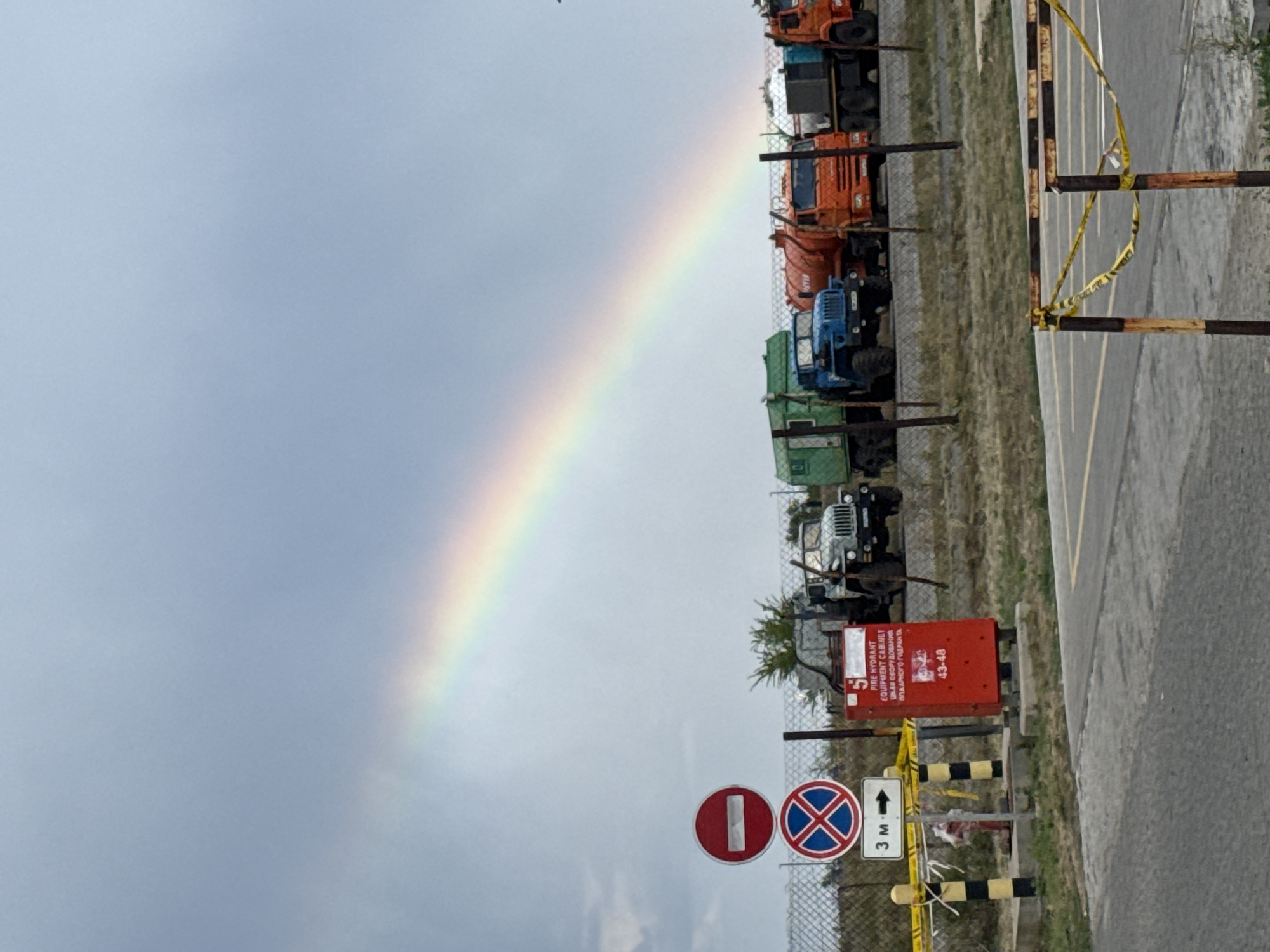 Rainbow over a rural Kazakh parking lot with trucks and SUVs