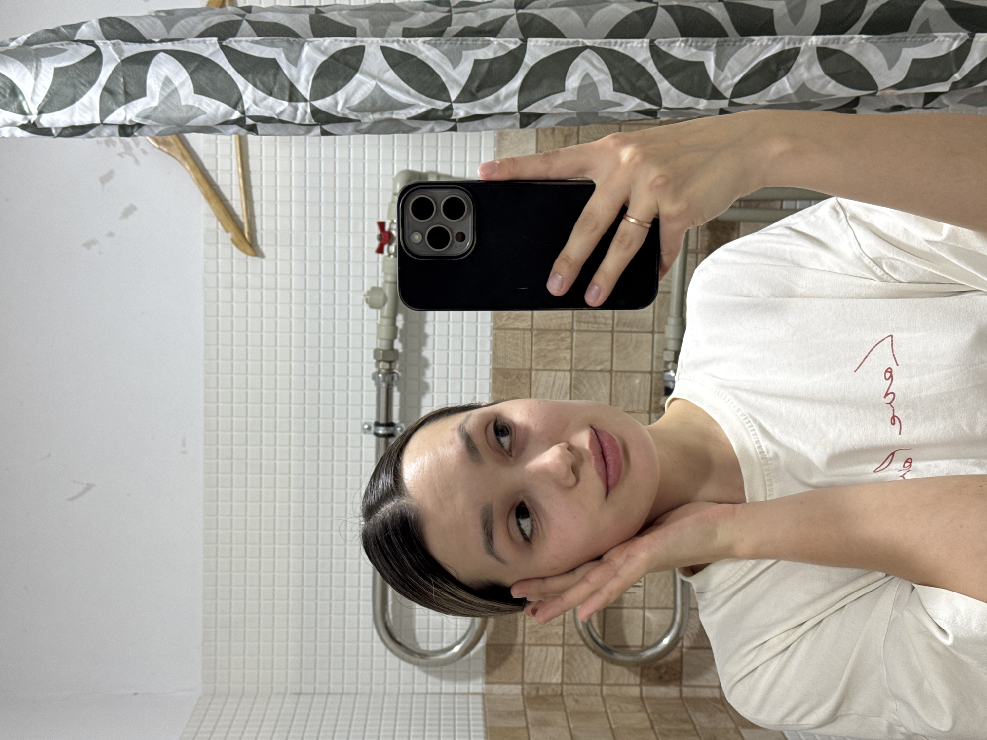Woman takes bathroom selfie with phone, gold ring visible