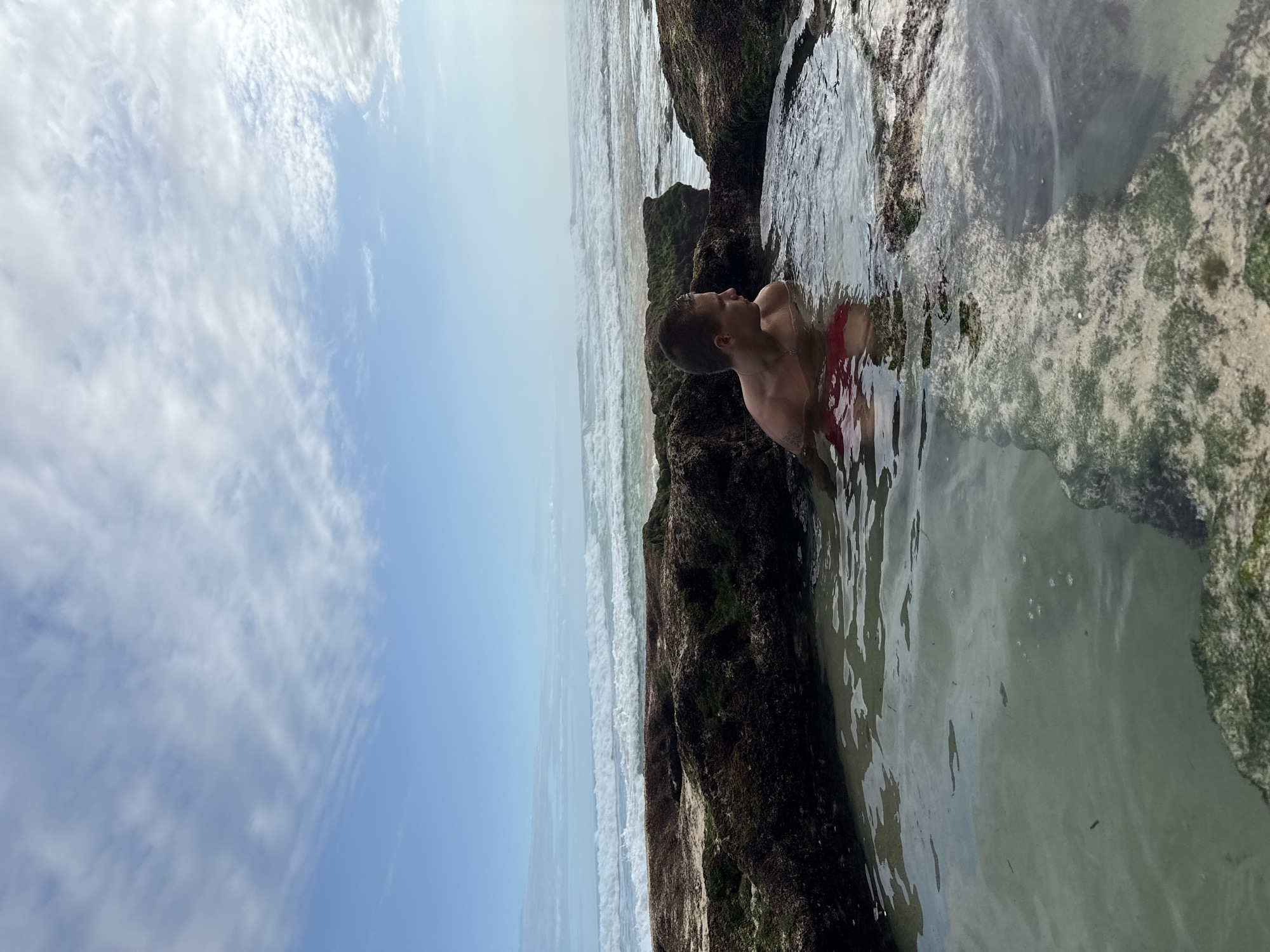 Man explores tide pools at rocky beach in Kuta Selatan