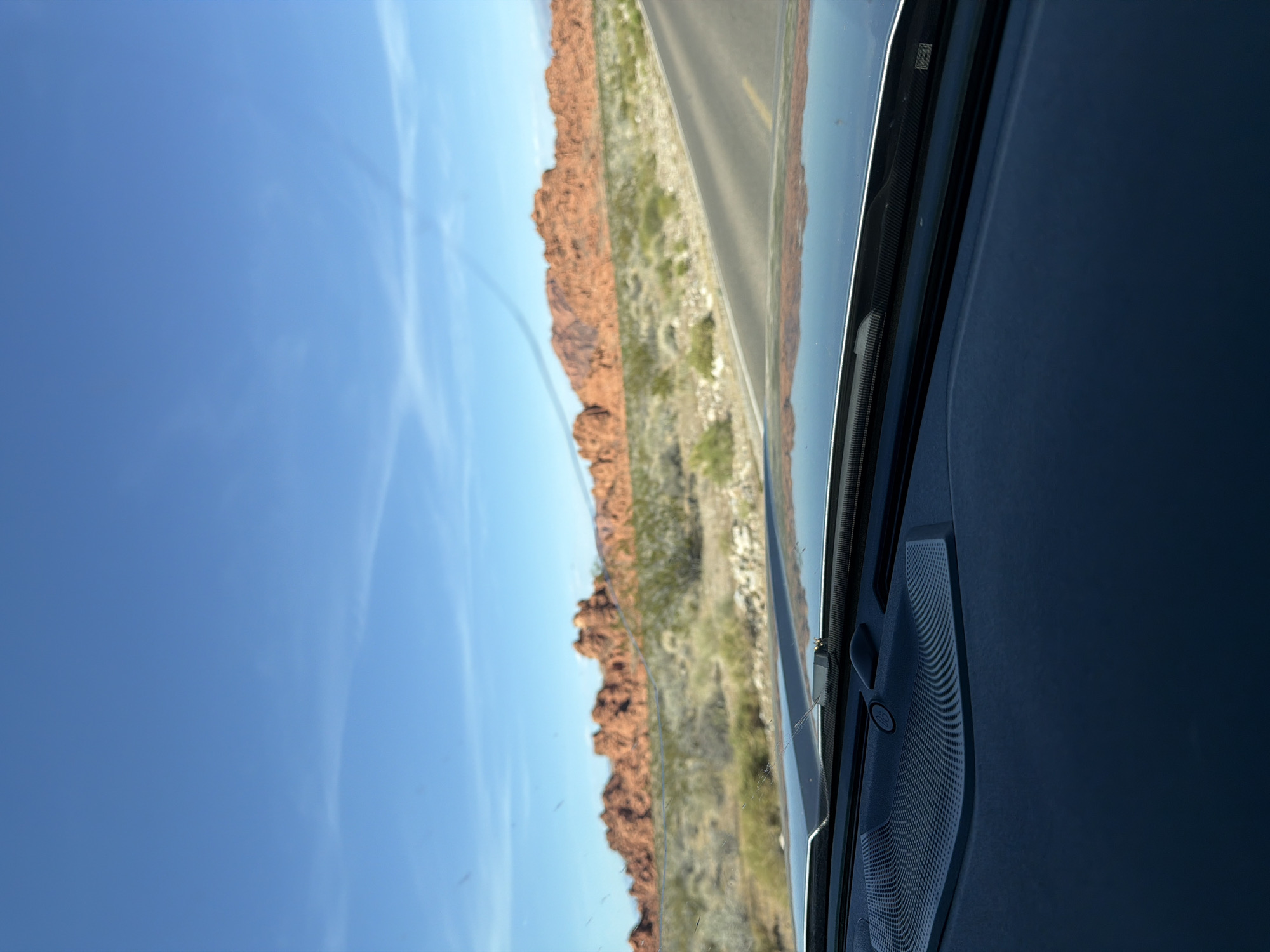 Driver captures desert landscape with red rocks through windshield