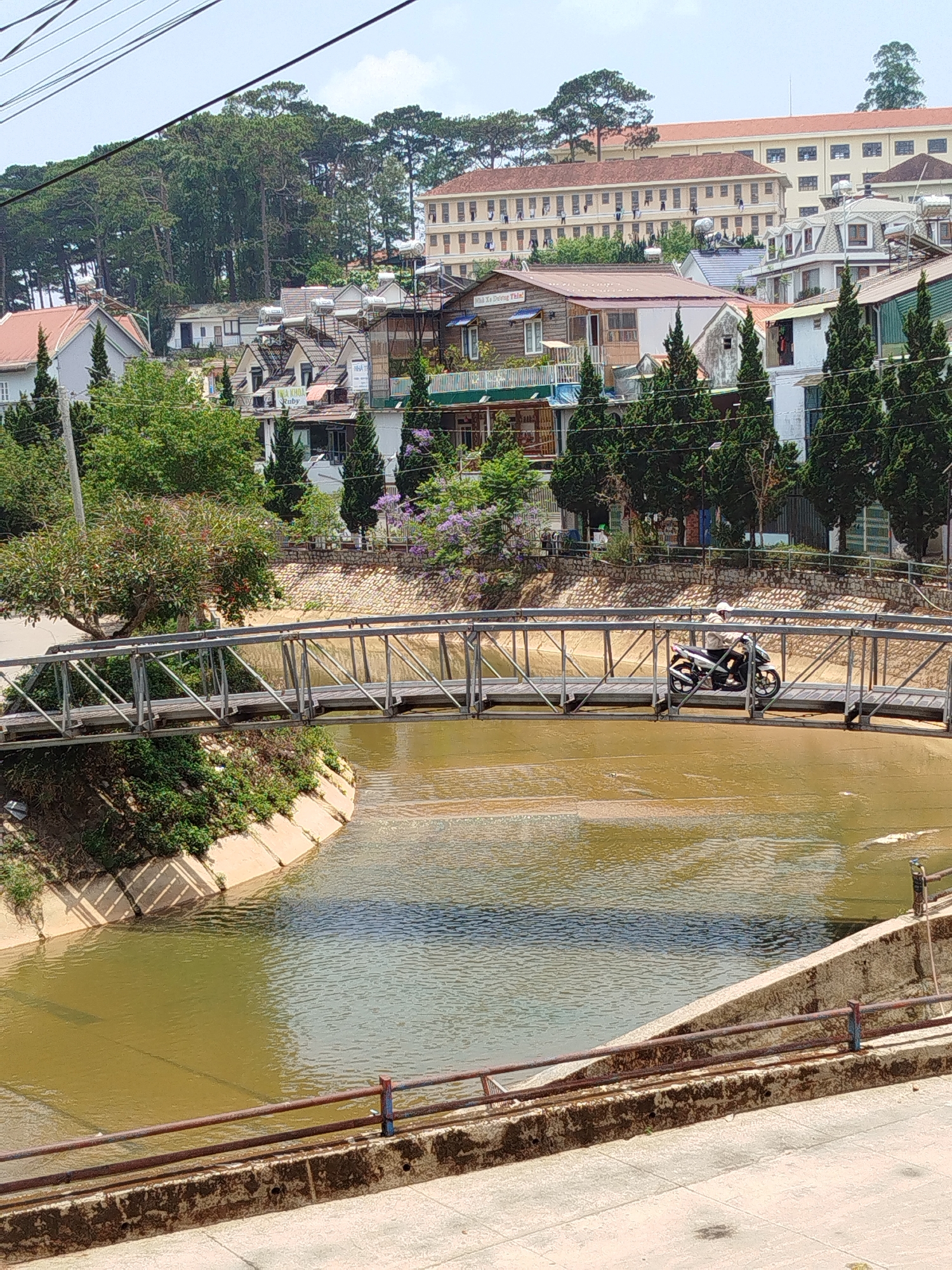 Morning motorbike traffic crosses canal bridge in Đà Lạt