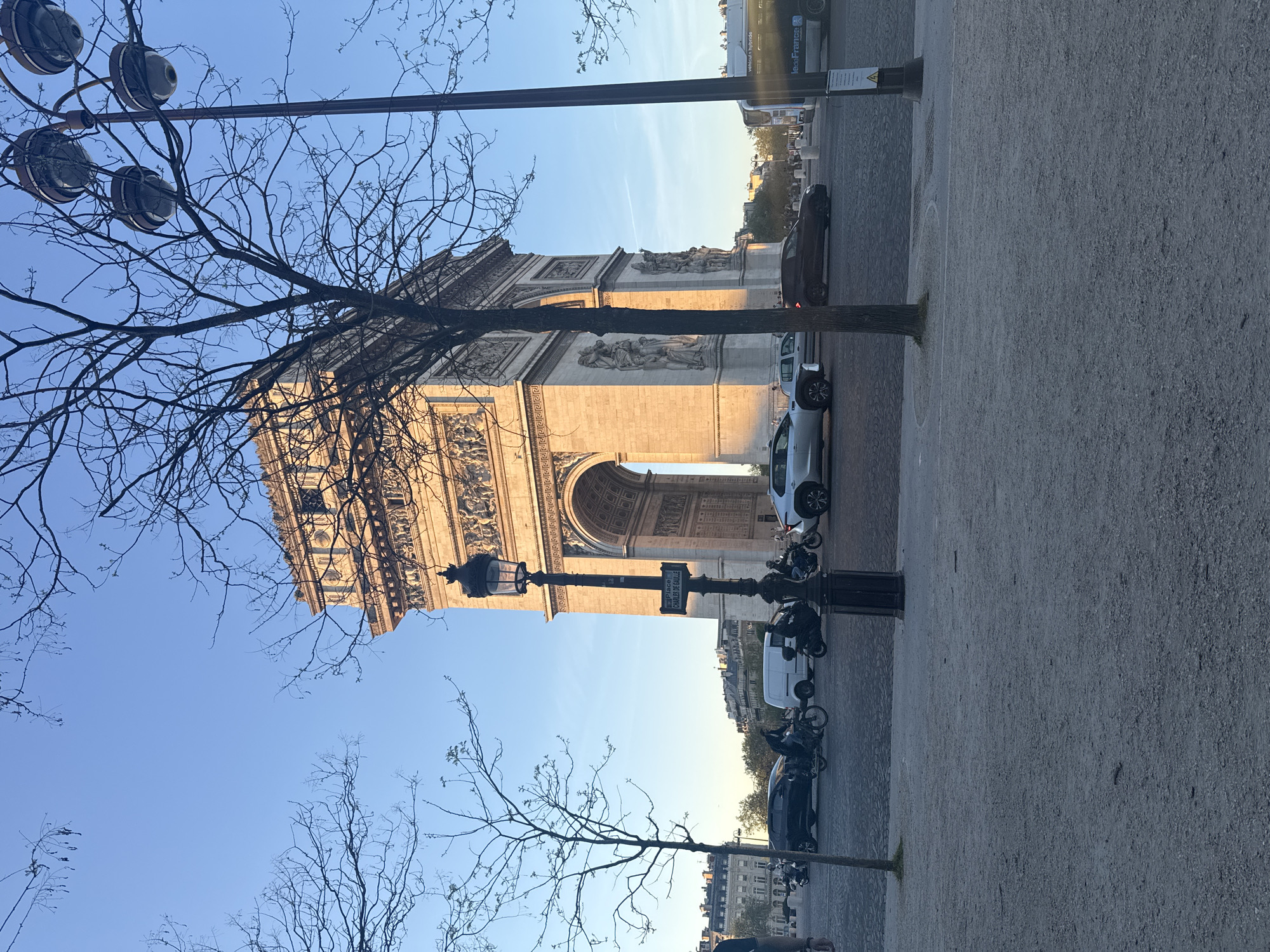 Arc de Triomphe photographed with parked vehicles, trees visible