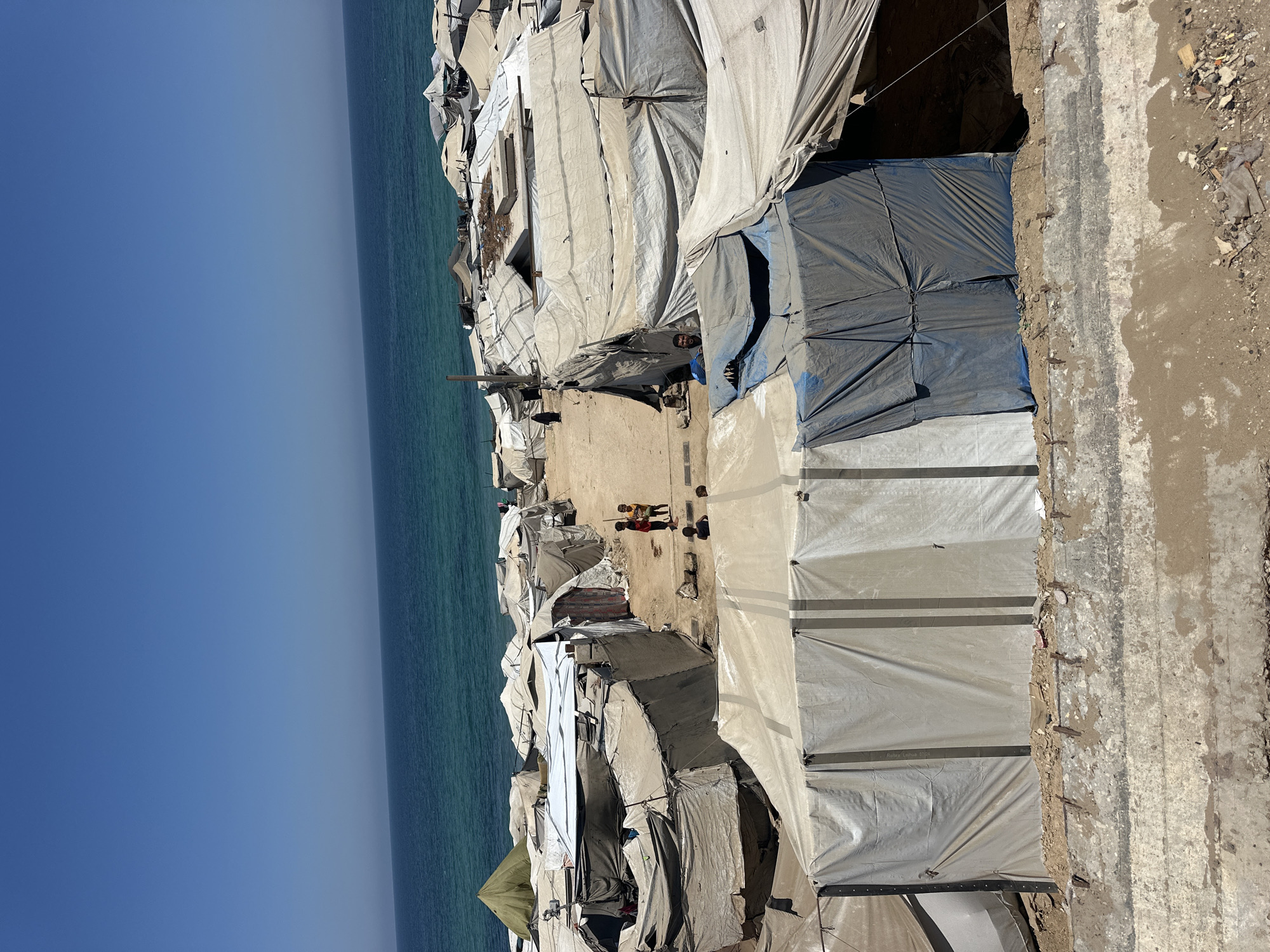 Coastal tent settlement with nearby beach activity and street markets