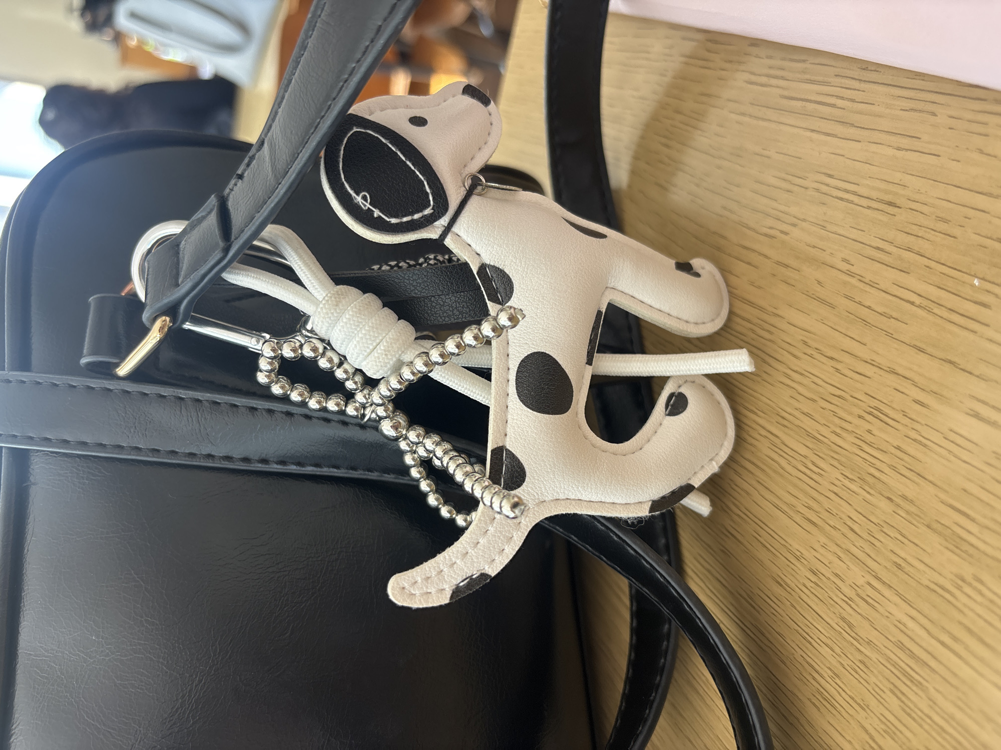 Black handbag spotted with Dalmatian-patterned keyring on wooden surface