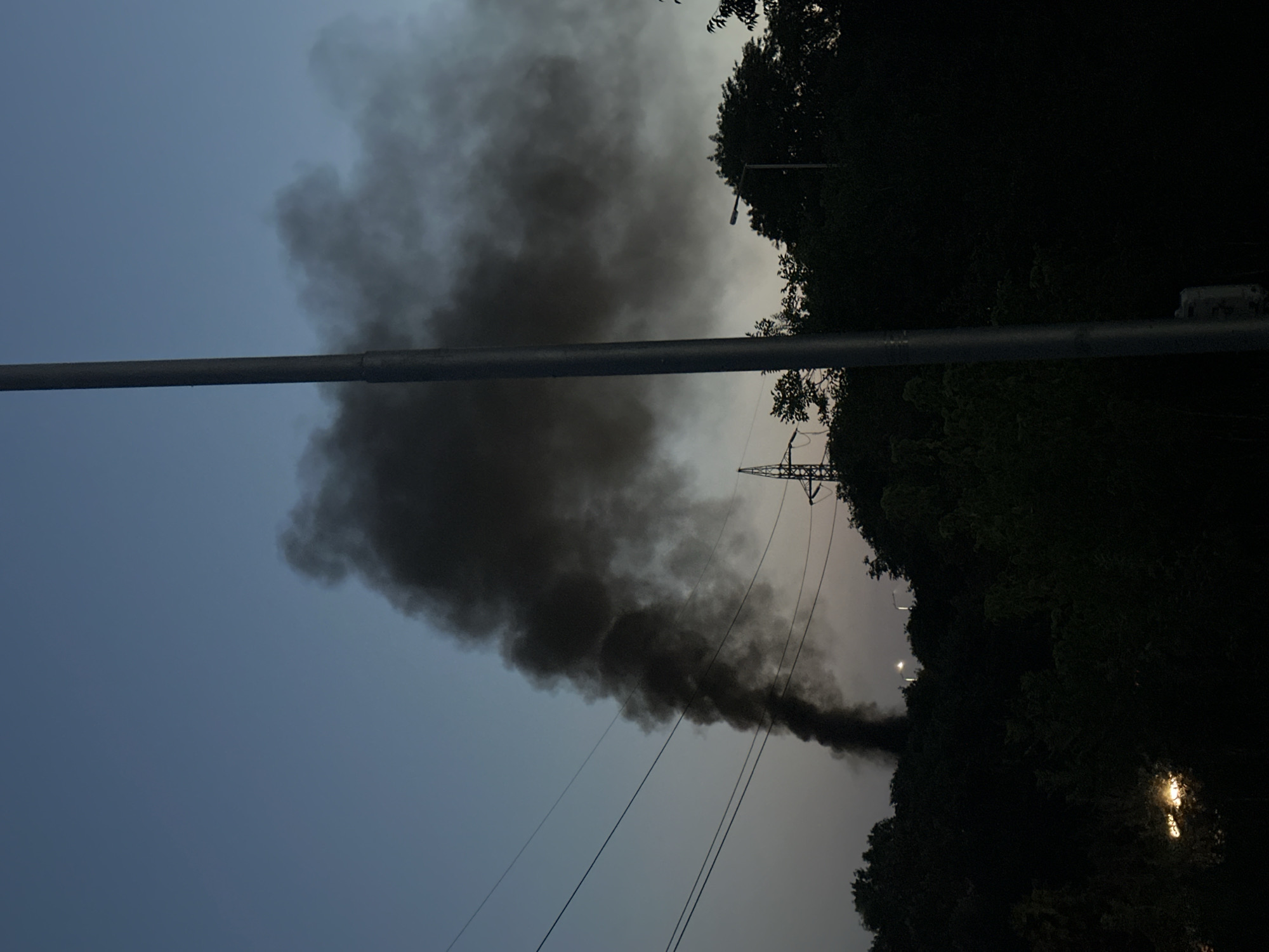 Dark smoke rising behind trees at dusk in Varna