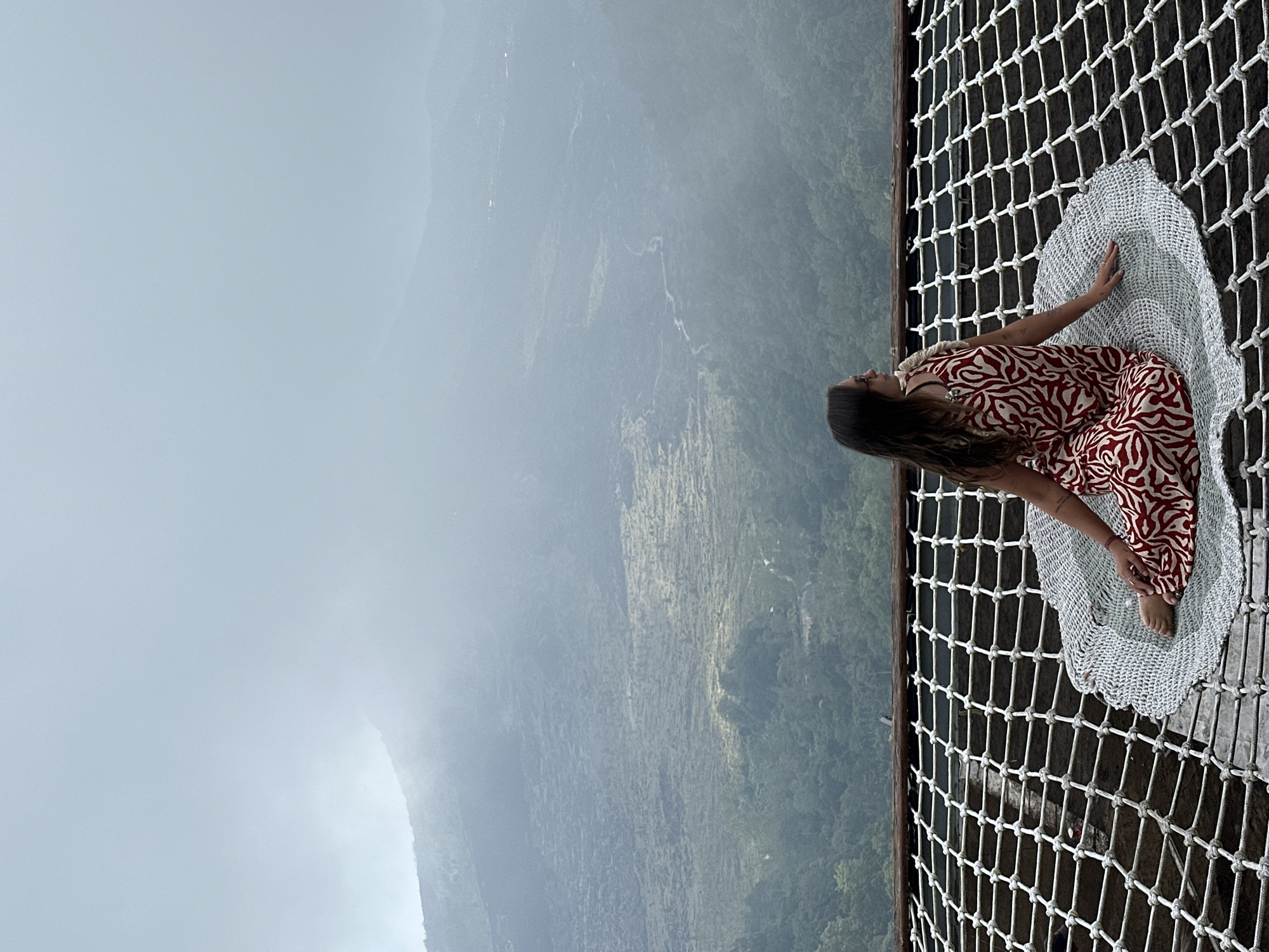 Woman sits on suspended net overlooking Kintamani mountains