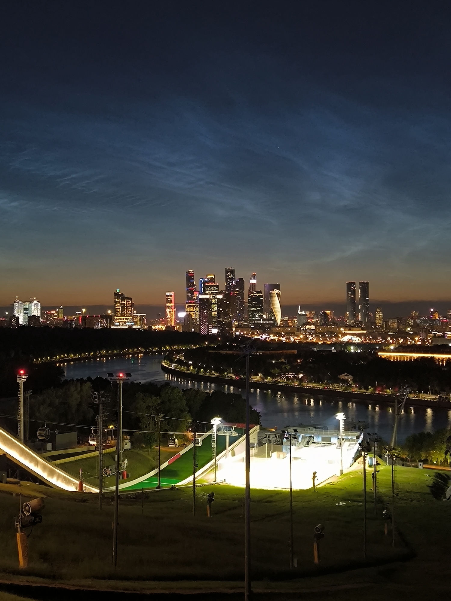 Illuminated ski jump at night with Moscow skyline behind it