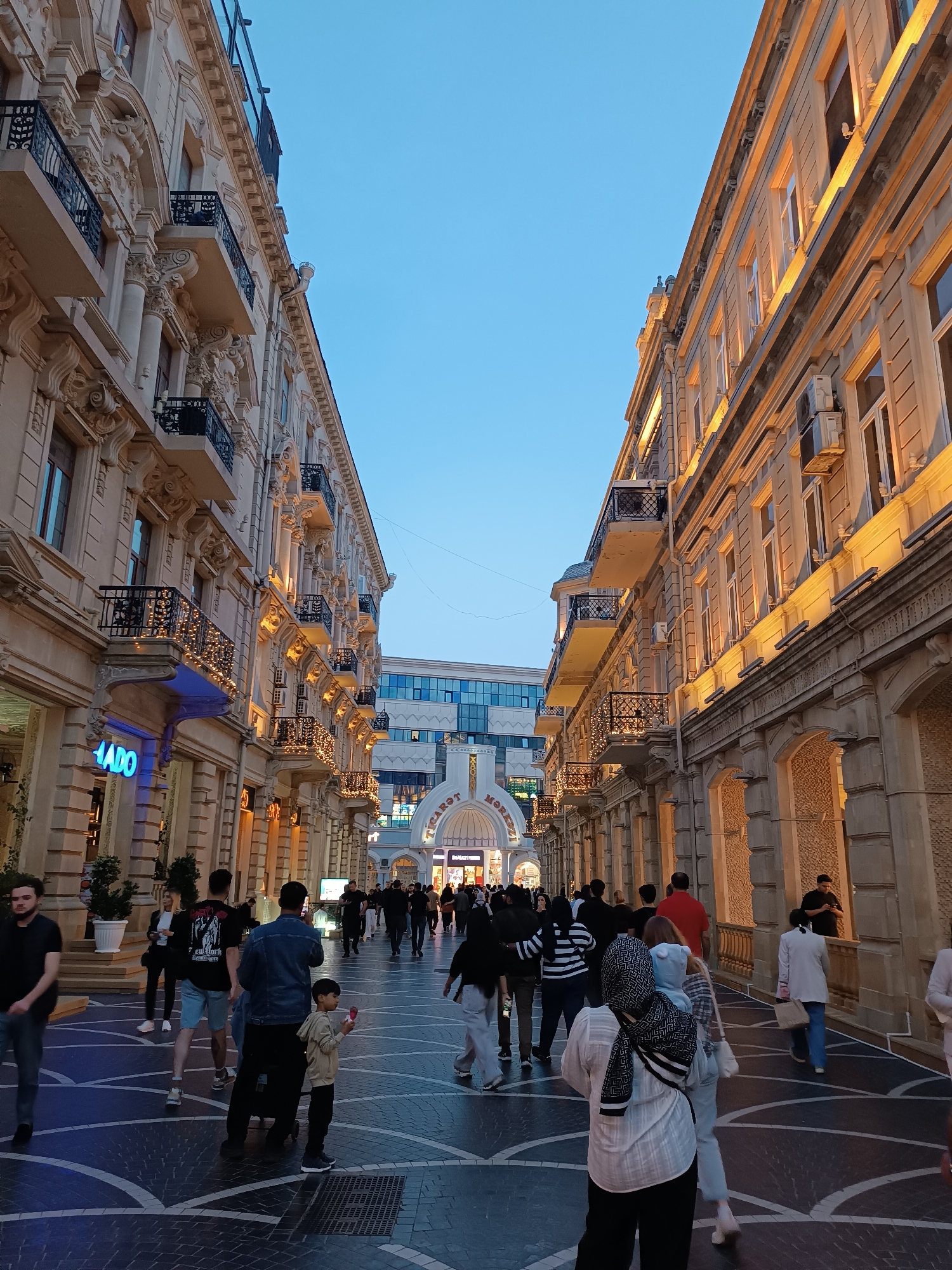 Evening pedestrians stroll illuminated historic street in Baku