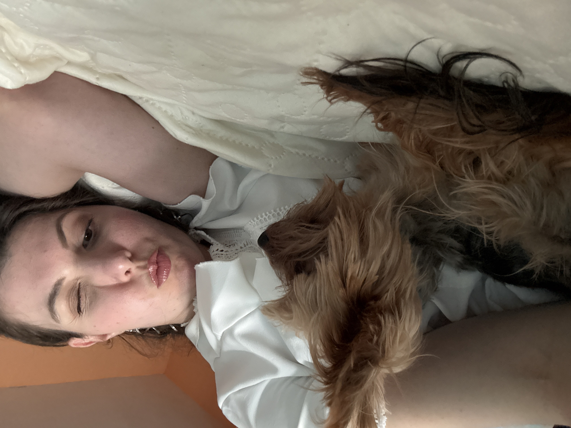 Woman takes selfie with small dog on bed